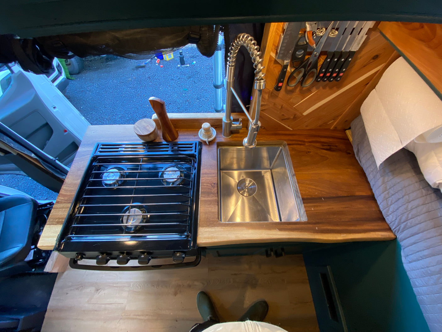 RV rental campervan kitchen: top-down view of gas stovetop, sink, and wood countertop. Knives and paper towels are visible, ready for travel.
