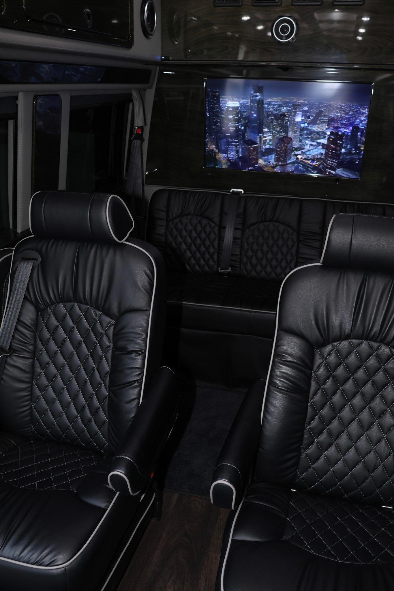 Spacious RV rental interior: luxurious black leather seats with quilted stitching, large TV displaying city lights.