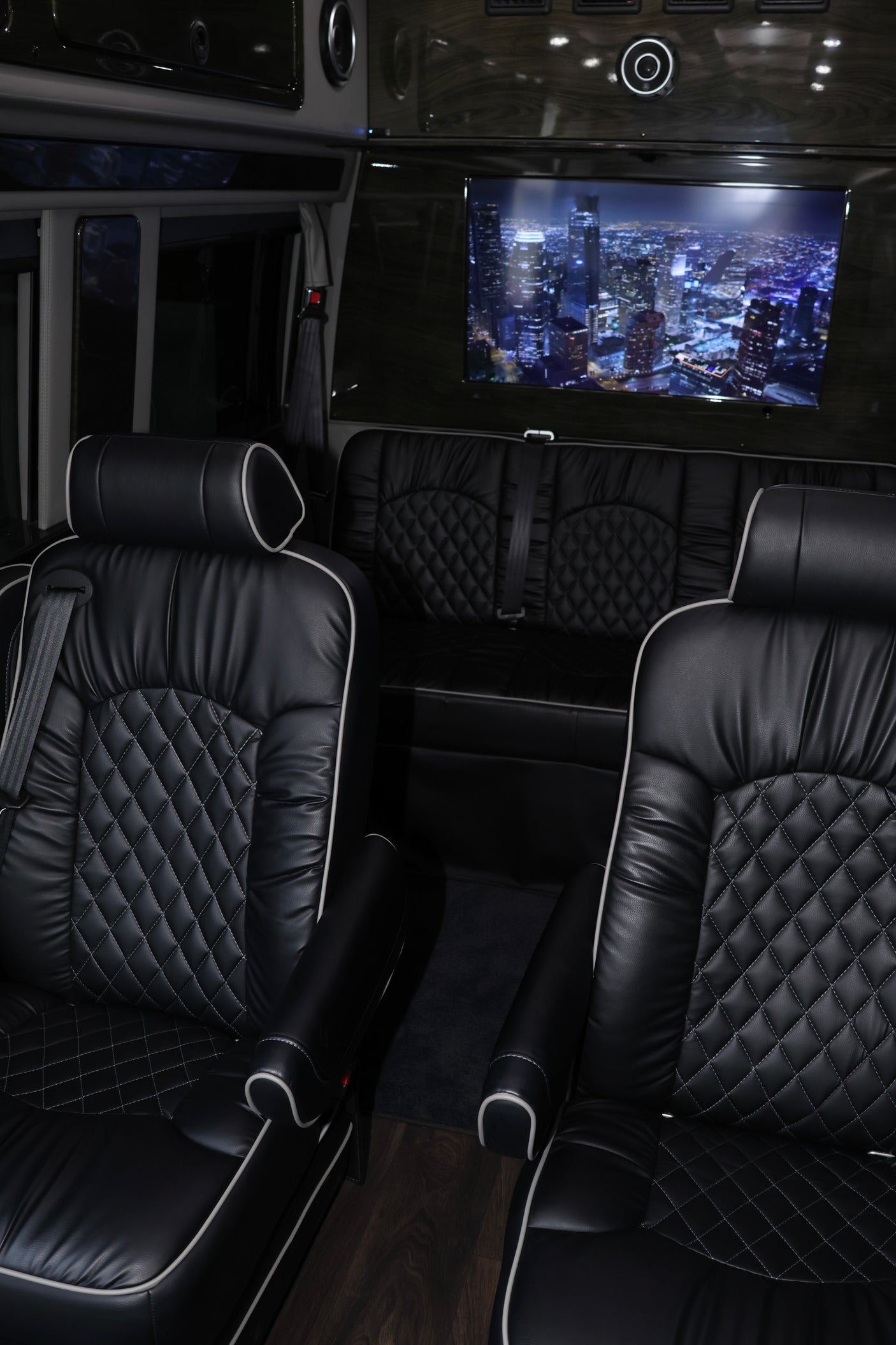 Spacious RV rental interior: luxurious black leather seats with quilted stitching, large TV displaying city lights.