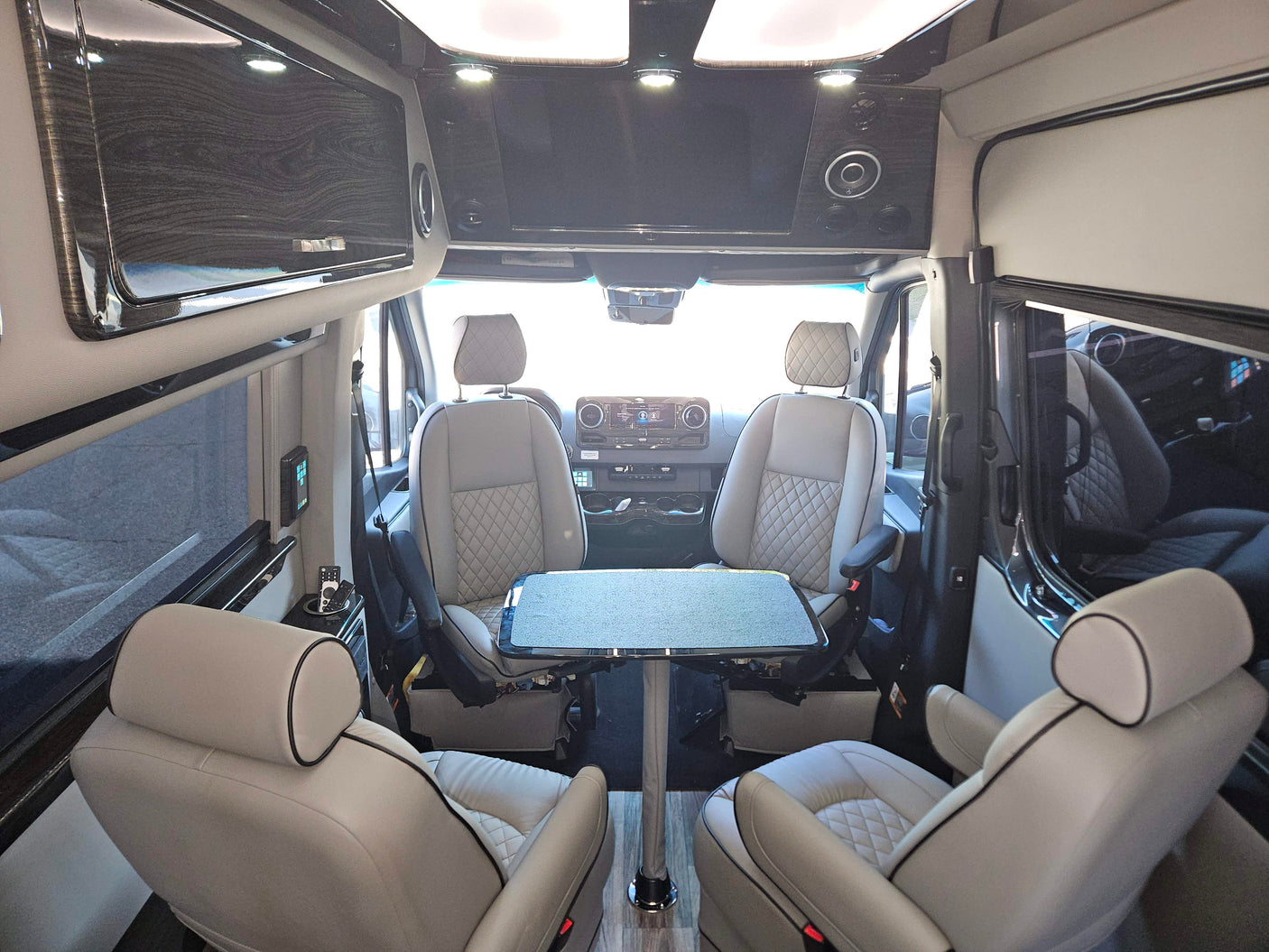 Luxury RV rental interior with comfortable captain's chairs, dining table, and overhead entertainment.