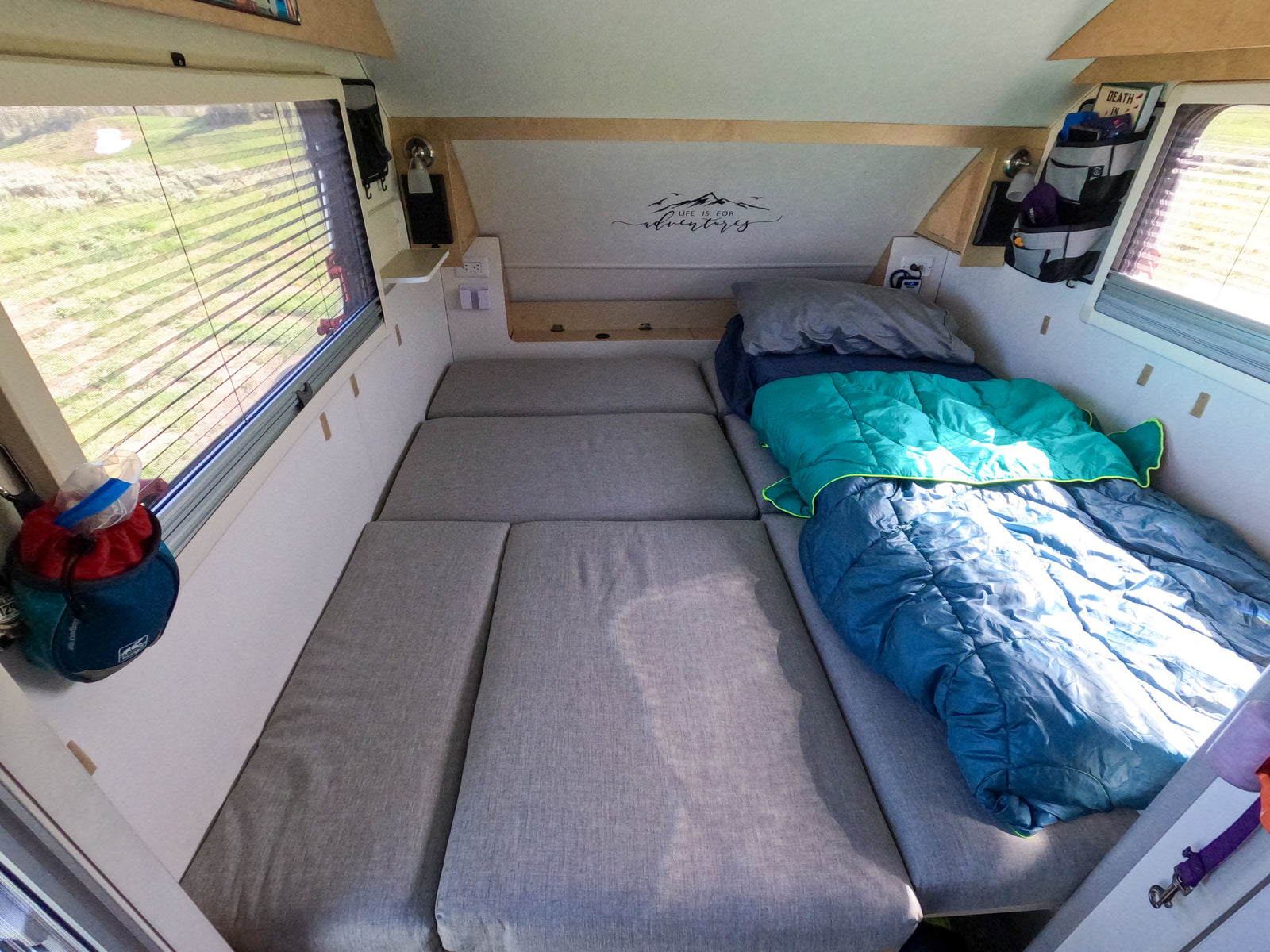 Inside an RV rental: a comfortable bed with sleeping bags, window view, and storage for your next adventure.
