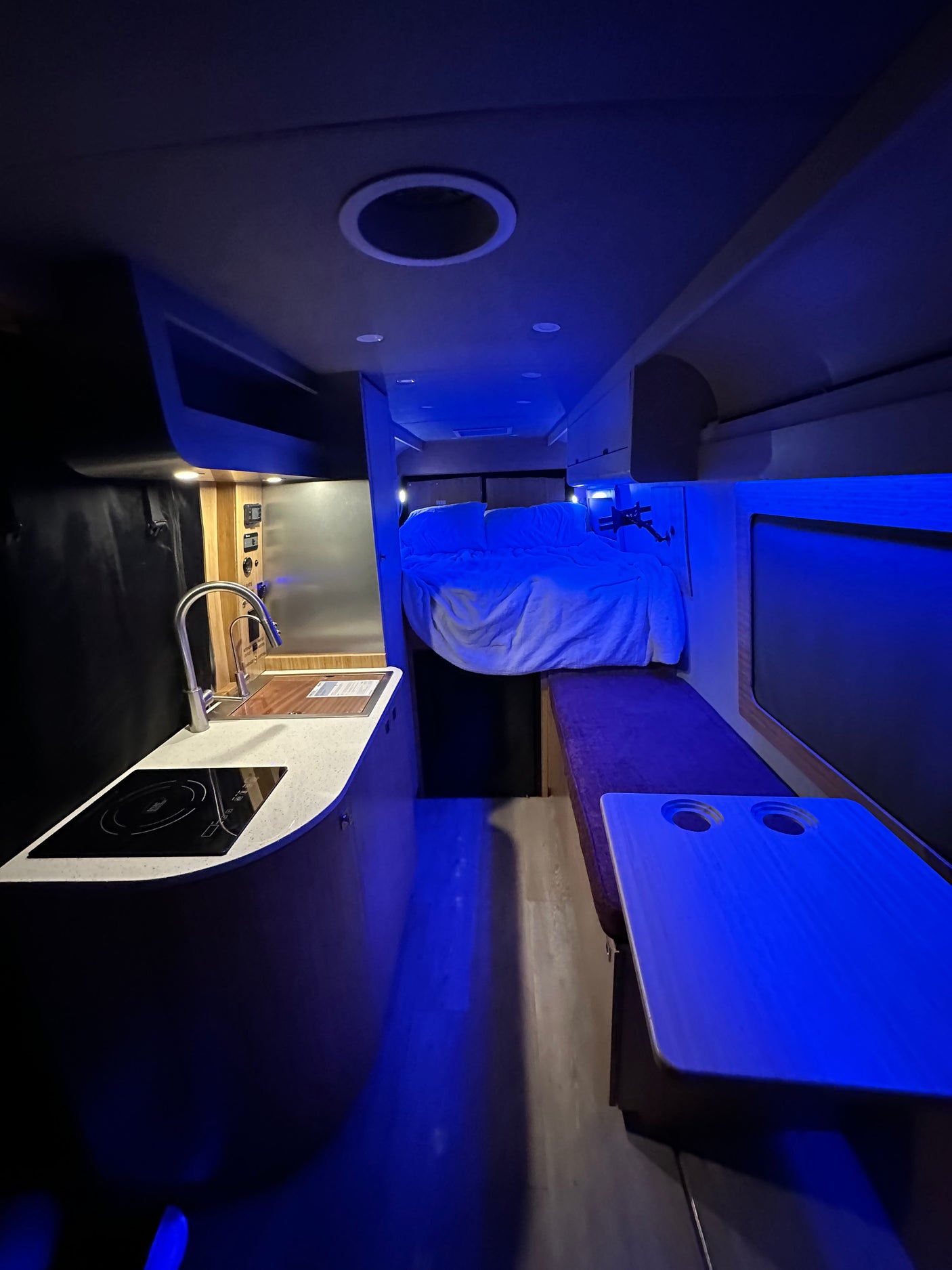 RV rental interior: A modern camper van setup with a functional kitchen, elevated bed, and striking blue ambient lighting.
