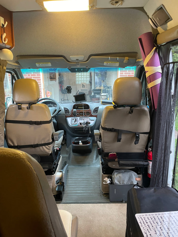RV rental interior view: the front cabin features tan swivel seats, a dashboard with controls, and travel essentials.