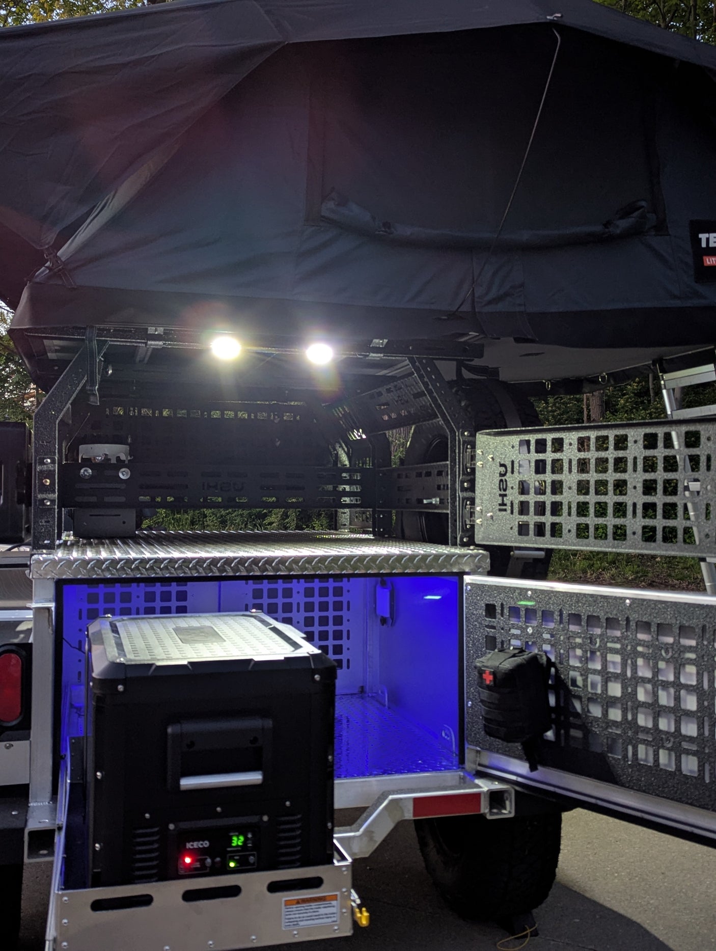 Off-road camper/rv rental setup: rooftop tent, bright lights, portable fridge, and illuminated gear storage.