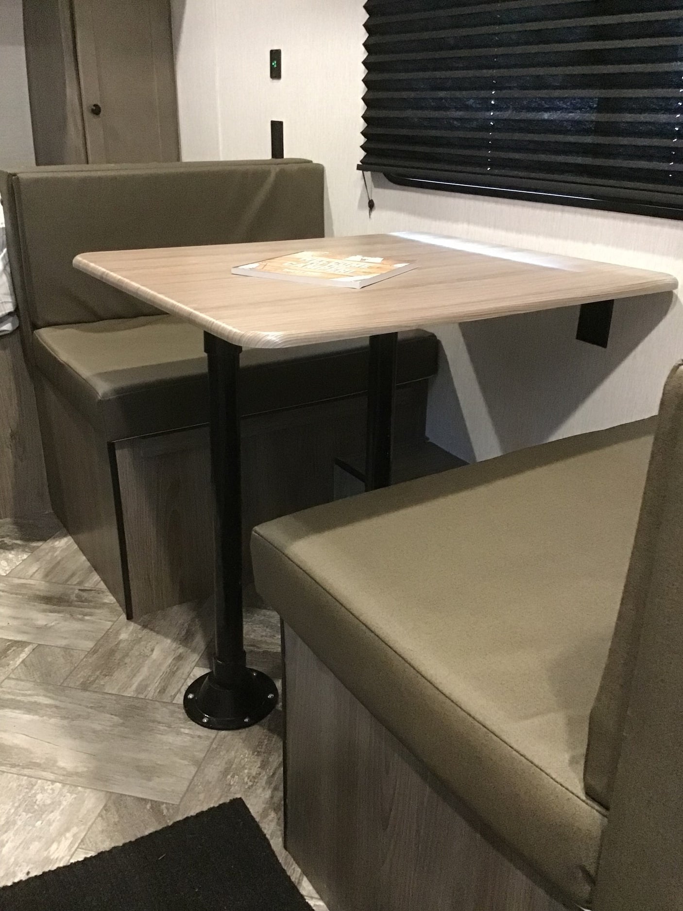 and mat at a shaded campsite.|Compact RV rental interior: view down a narrow aisle towards a bunk bed