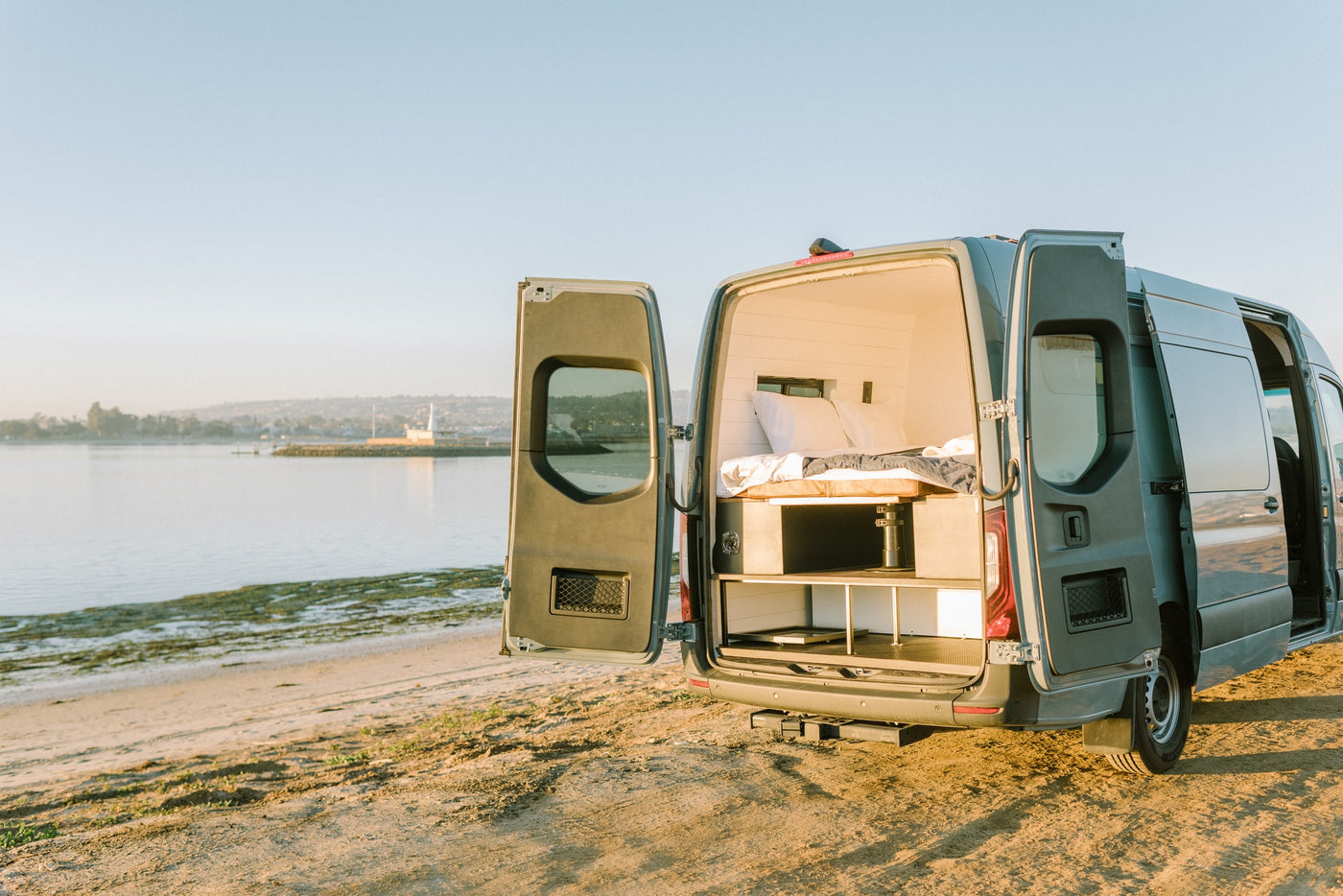 Scenic RV rental parked on a sandy beach at golden hour, revealing its comfortable bed and storage in the back. — photo 11