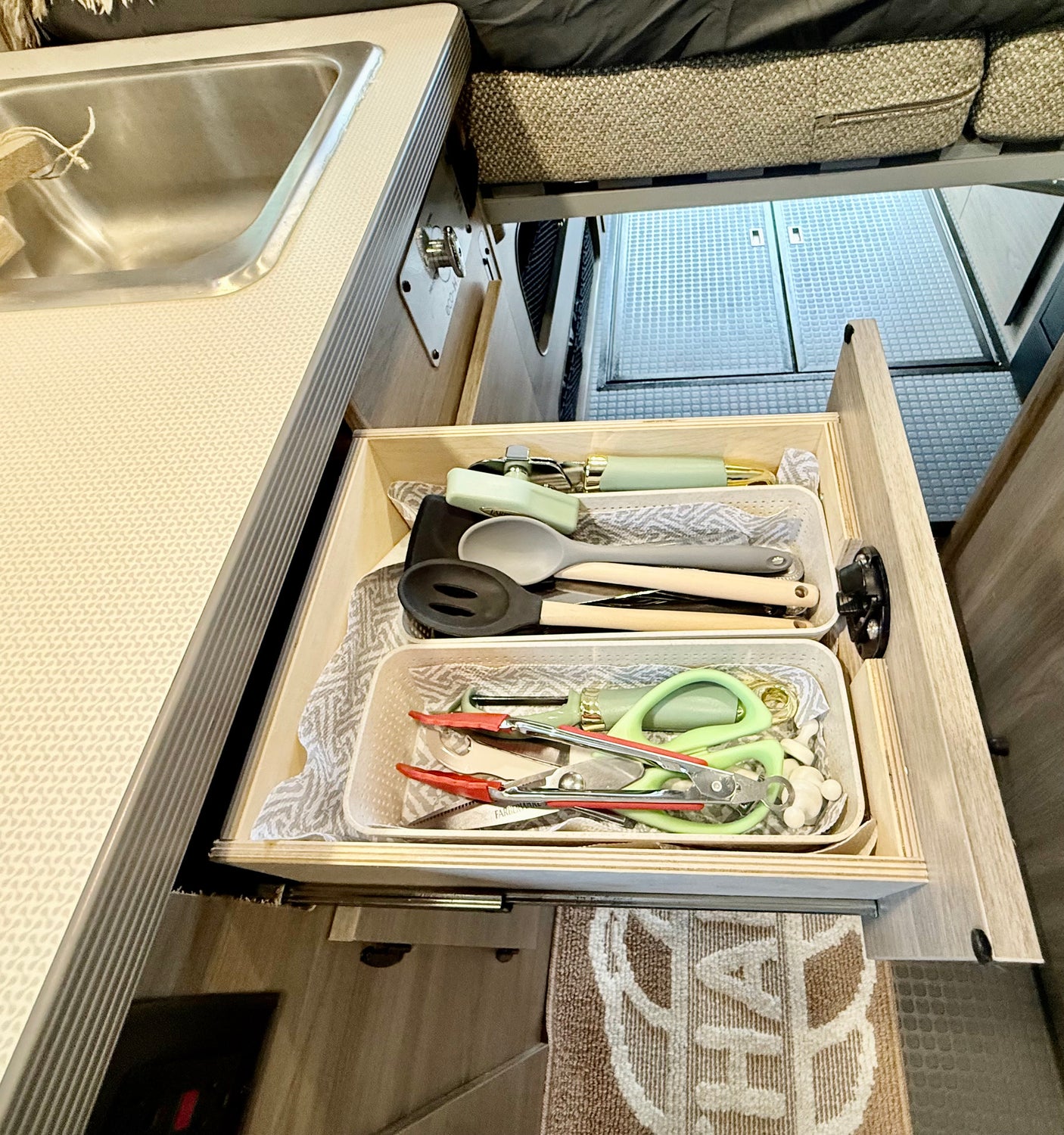 Open RV rental kitchen drawer with light green/grey utensils, next to a stainless steel sink and patterned counter.