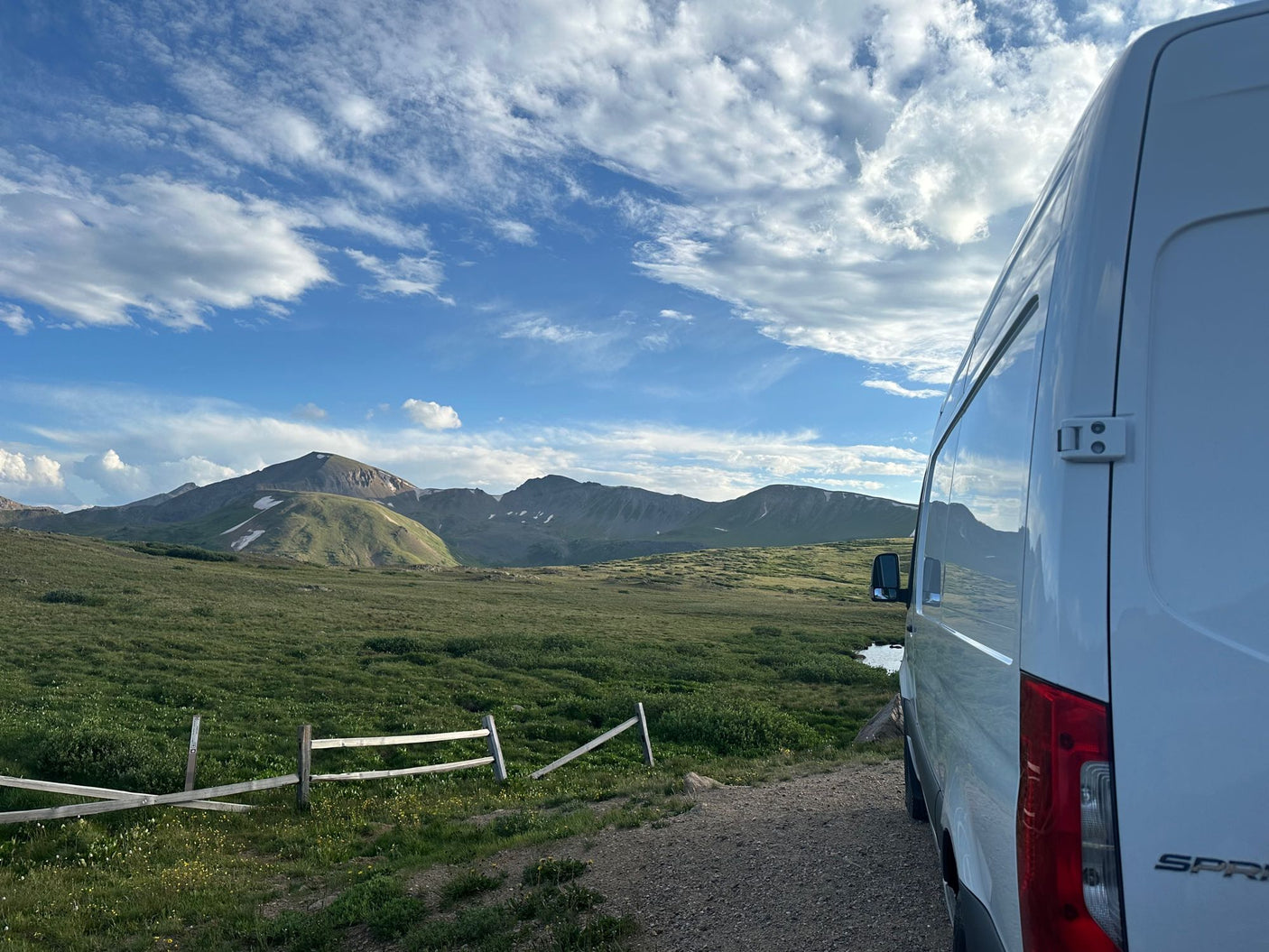 Scenic RV rental trip: A white van parked on a dirt road overlooking vast green mountains under cloudy skies.