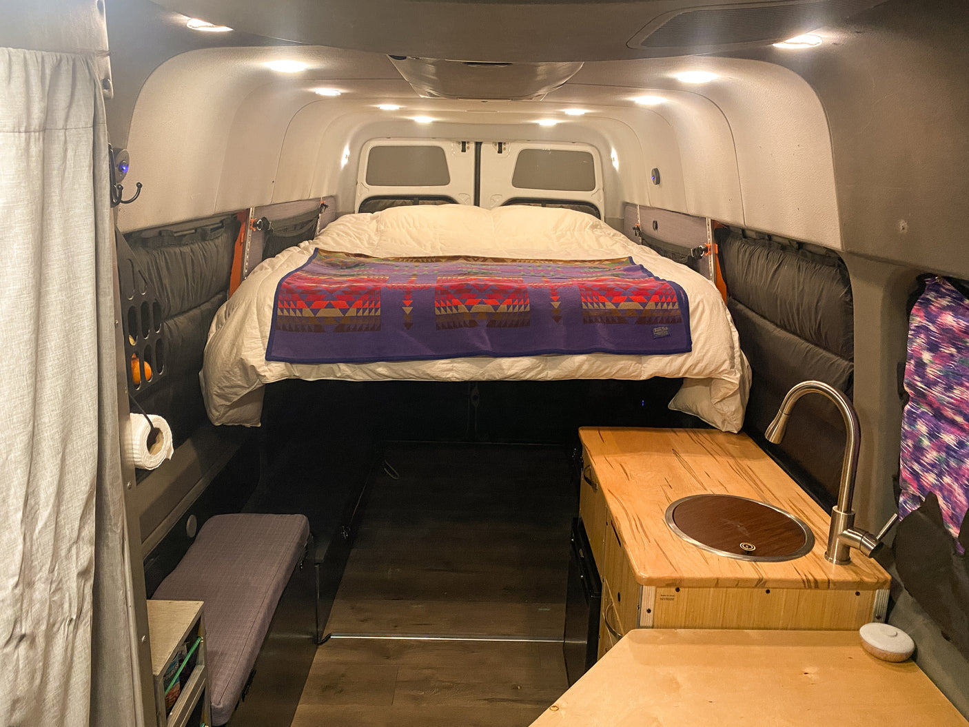 Custom RV rental interior: bed, compact kitchen with sink, and clever storage solutions for van life comfort.