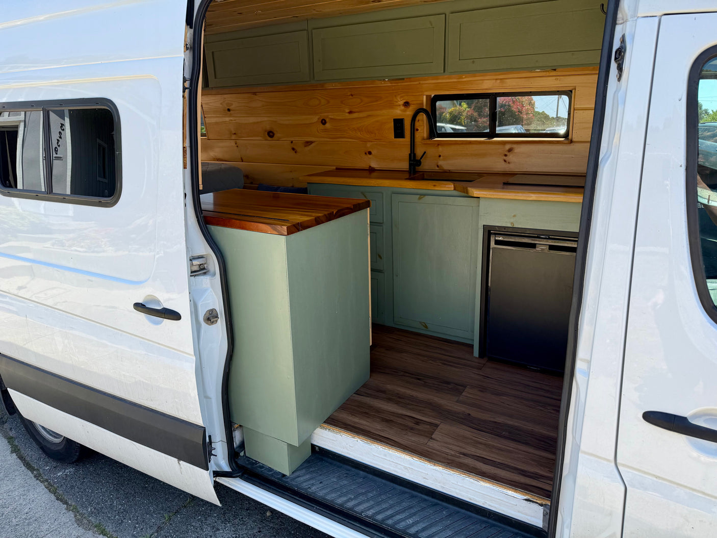 White camper van conversion interior: wood, green cabinets, sink, fridge. Great for RV rental!