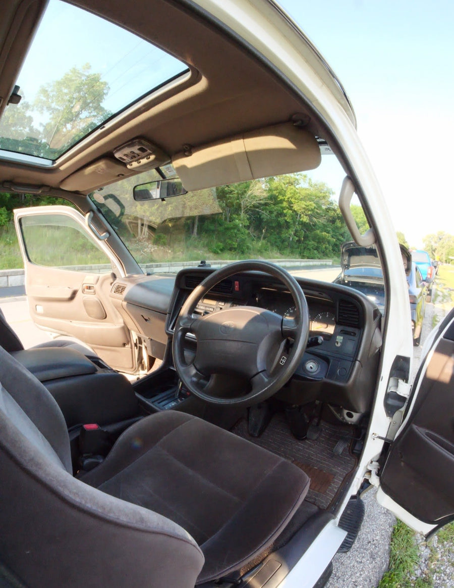 open by a lake for outdoor adventure. Other vehicles and a fishing rod are present.|White Toyota van