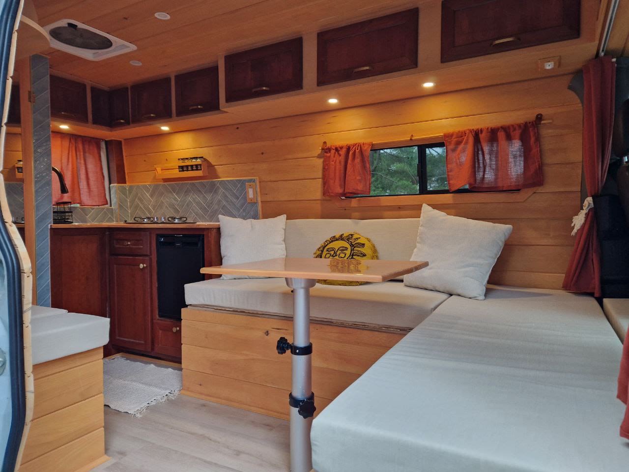 showcasing its custom wood interior through the open side door.|Explore this cozy RV rental's wooden interior: a kitchenette