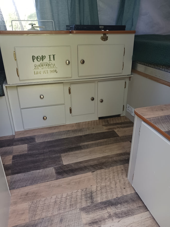 This inviting RV rental interior showcases custom light-colored cabinets, wood-look flooring, and a playful 'POP IT' graphic.