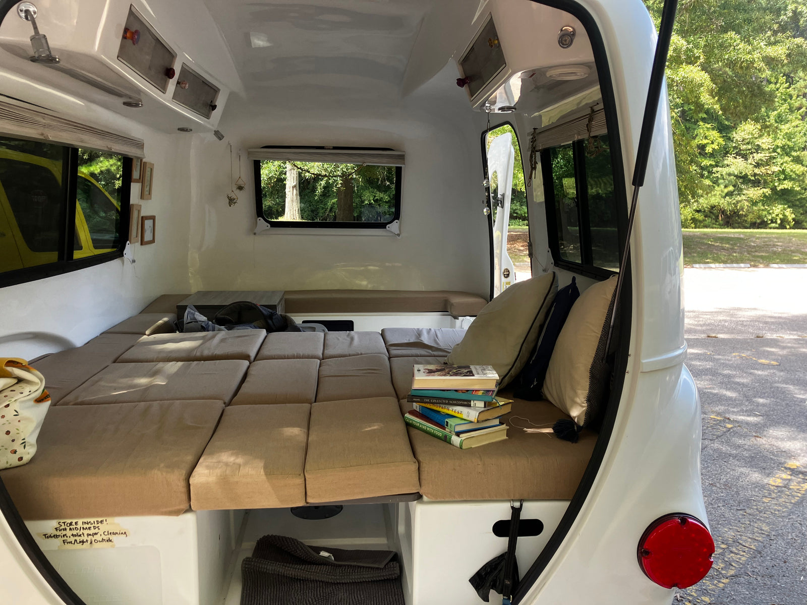 Inside a compact RV rental: a plush bed, stack of books, and smart storage solutions for travelers.