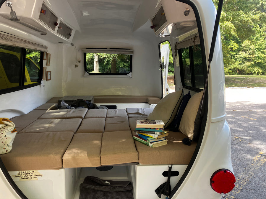 Inside a compact RV rental: a plush bed, stack of books, and smart storage solutions for travelers.