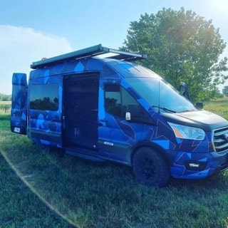 A blue camo-patterned camper van with open doors in a sunny field. Perfect for your next RV rental adventure!