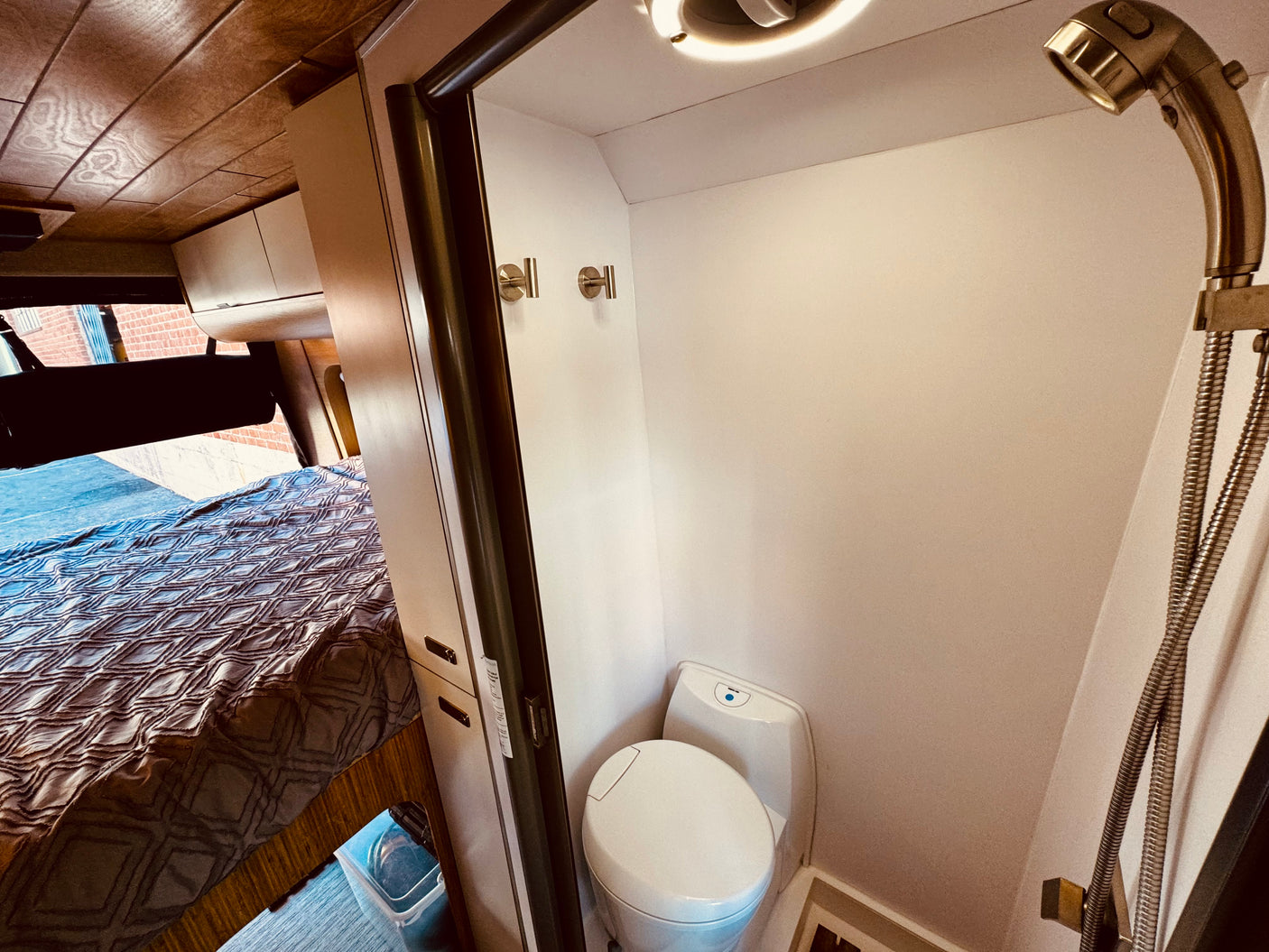 Cozy RV rental interior showcasing a patterned bed, and a compact wet bath with a modern toilet and shower.