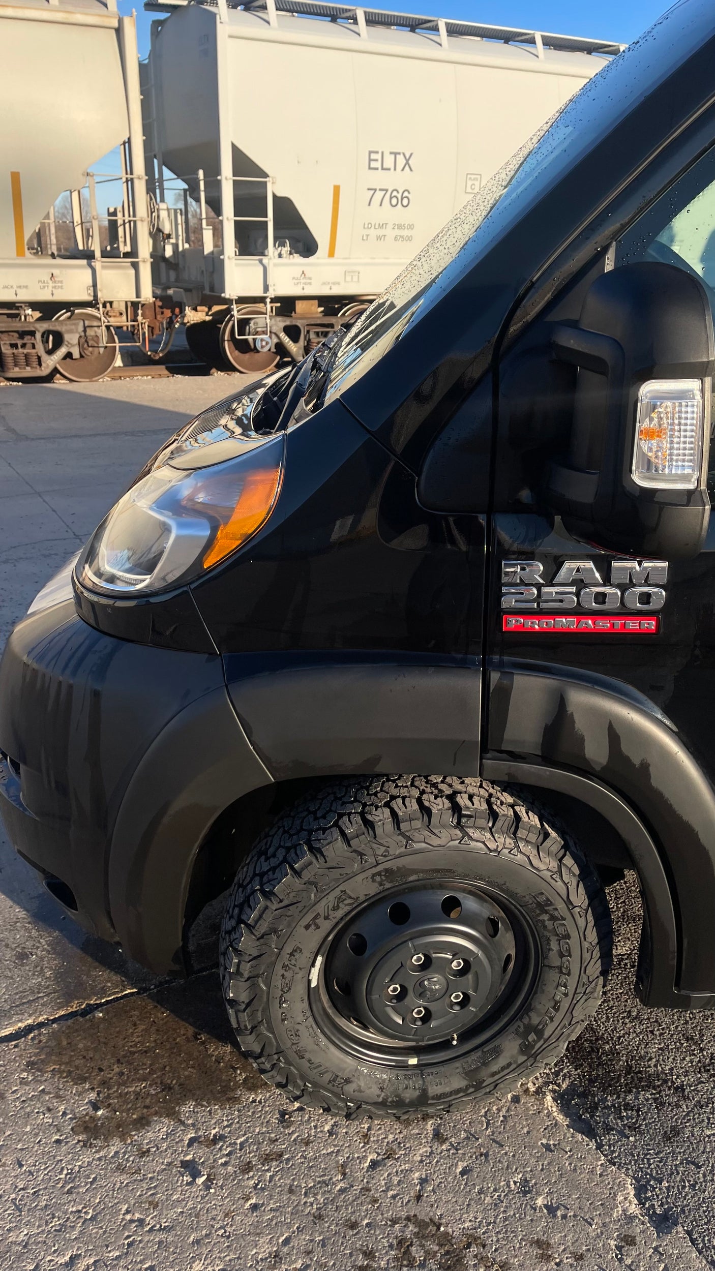 Black Ram ProMaster 2500 van with rugged tires, ideal for an rv rental adventure, parked by train cars.