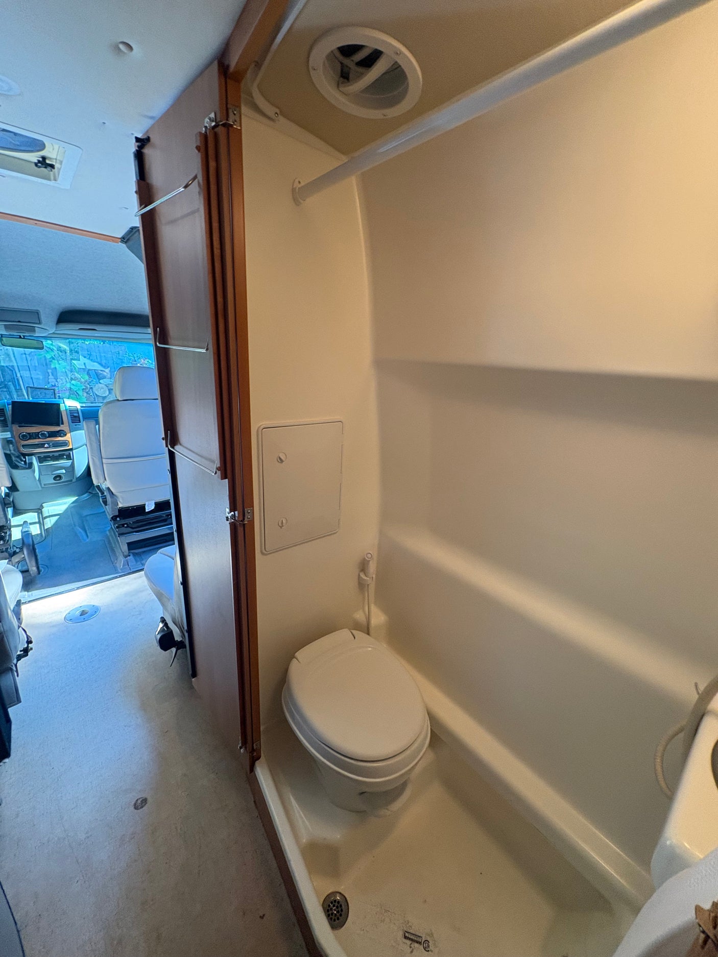 RV rental wet bath interior showing toilet, shower, and ceiling vent. Bifold door partially open to RV cockpit.