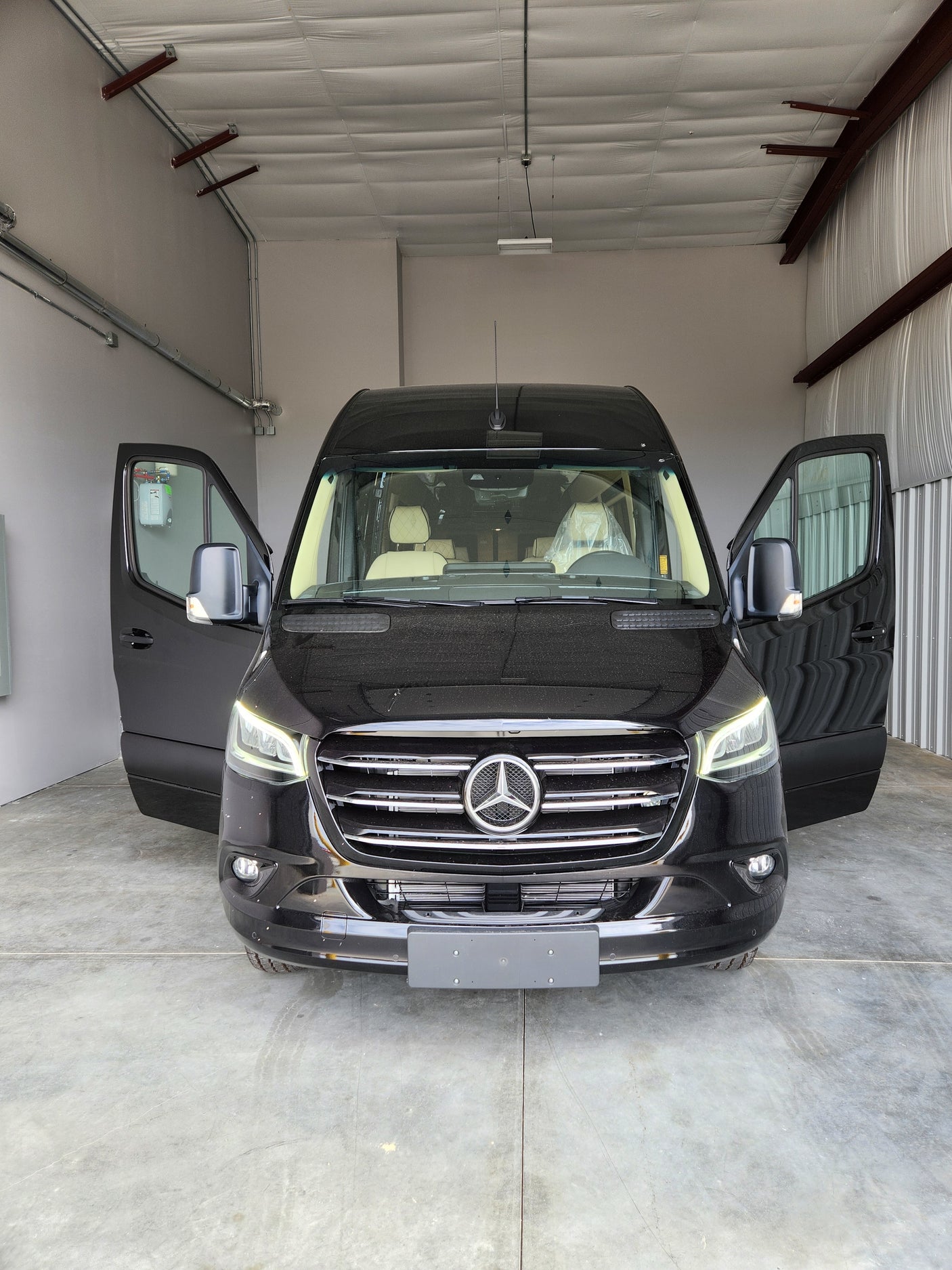 Discover this new black Mercedes-Benz Sprinter van, perfect for rv rental. Front doors open, showcasing a luxurious interior.