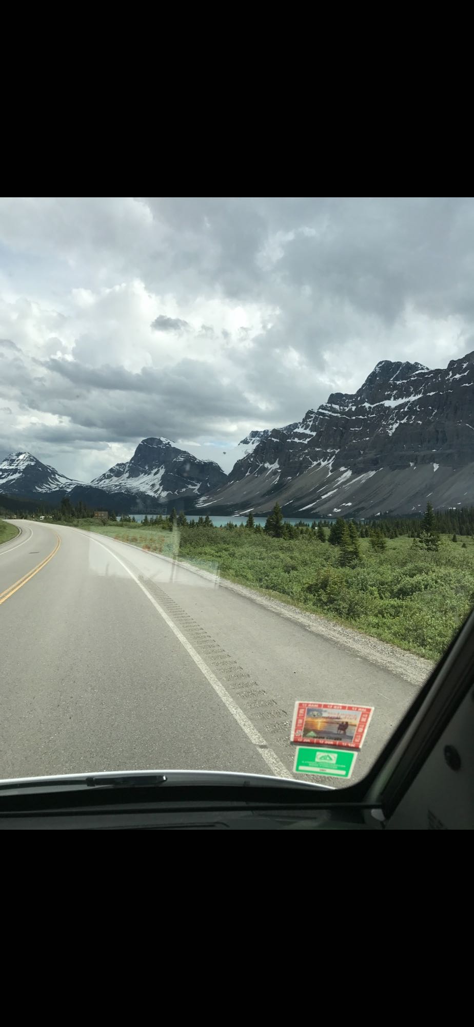 Scenic RV rental drive through Canadian Rockies, featuring snow-capped mountains, winding road, and turquoise lake.