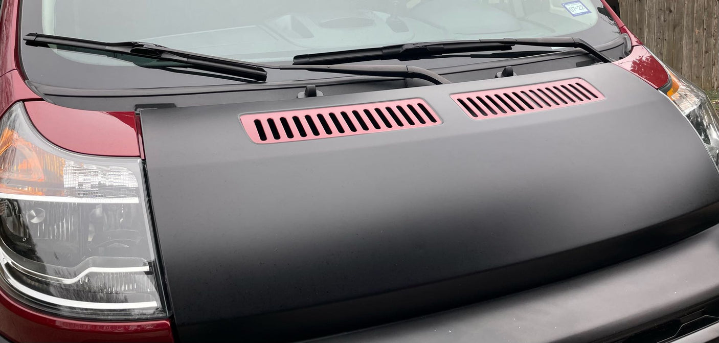 Front view of an RV rental with a matte black hood, prominent pink vents, and a red body section visible.