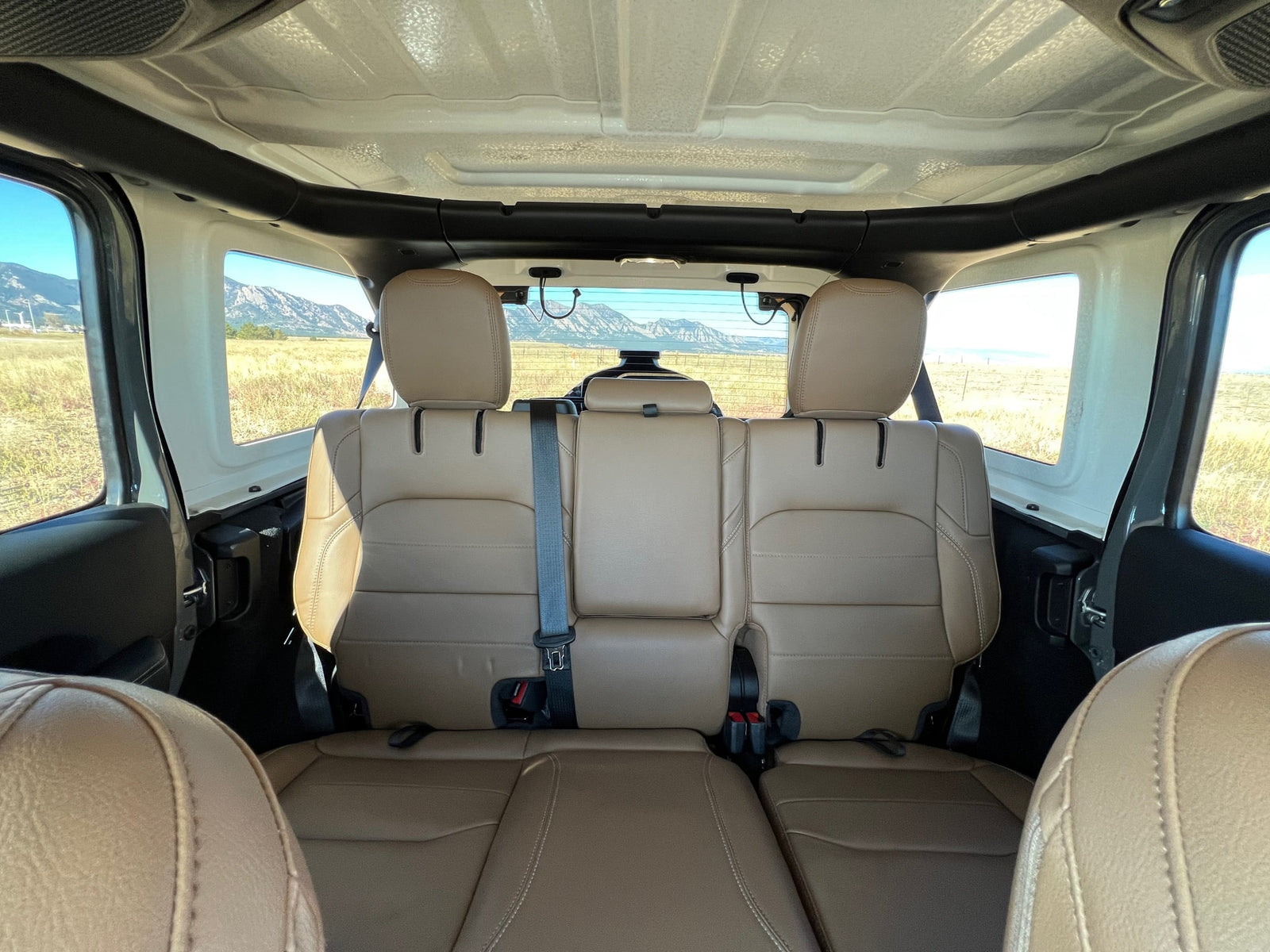 Comfortable tan rear seats of an RV rental offer panoramic views of scenic fields and mountains.