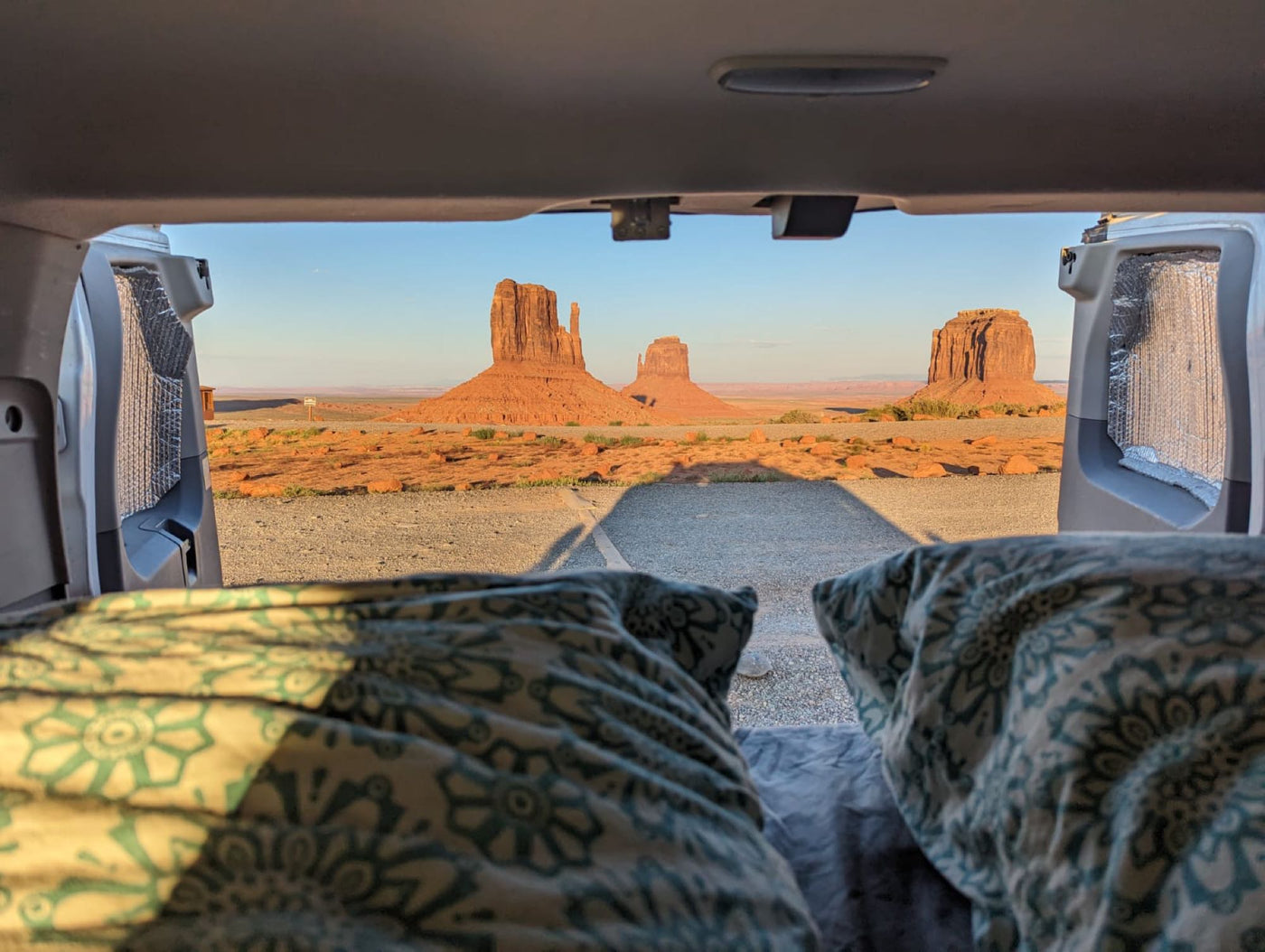 nestled in lush green hills.|RV rental van's interior: an elevated bed with a white mattress & patterned pillow — photo 2