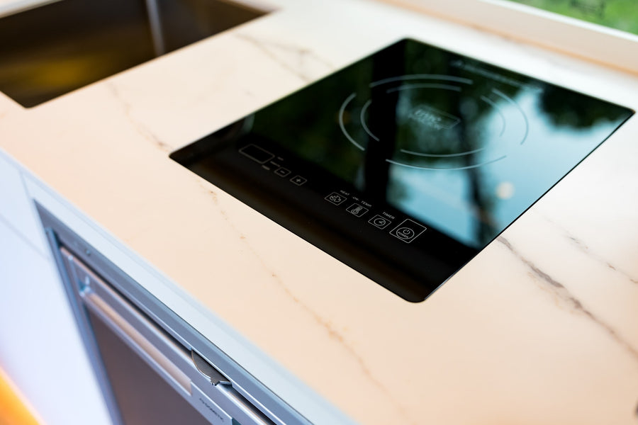 Modern RV rental kitchen with a sleek induction cooktop, sink, marble countertop, and Dometic fridge drawer.