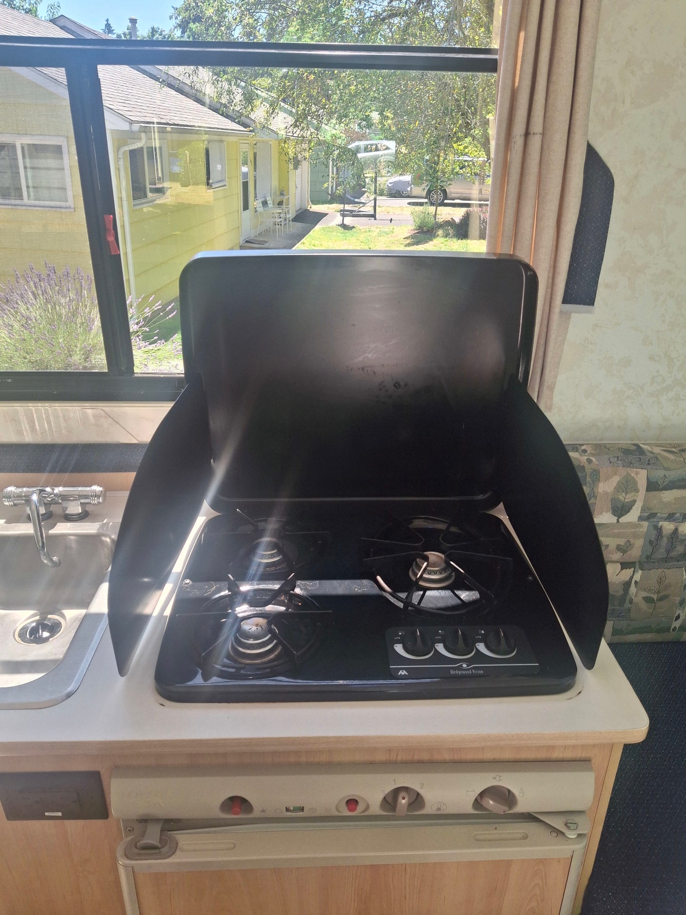 Functional RV rental kitchen with a gas stove, sink, and bright window offering an outdoor view.