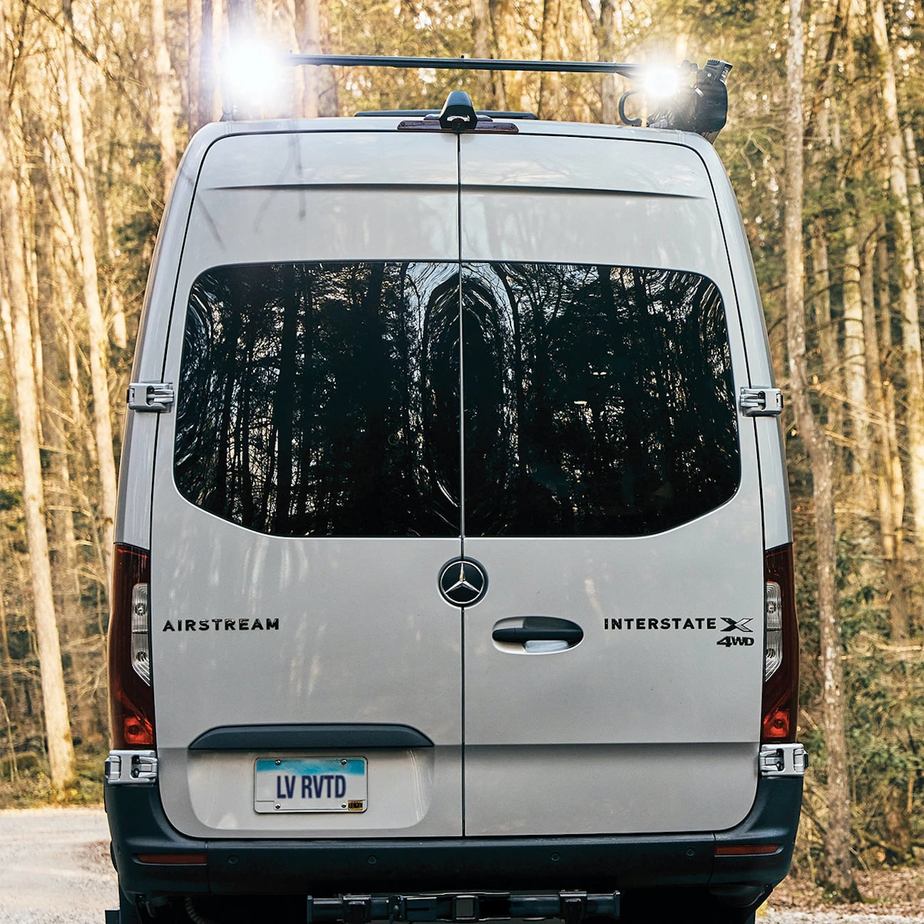 Rear view of a silver Airstream Interstate X 4WD Mercedes RV in the woods. Perfect for an rv rental adventure!