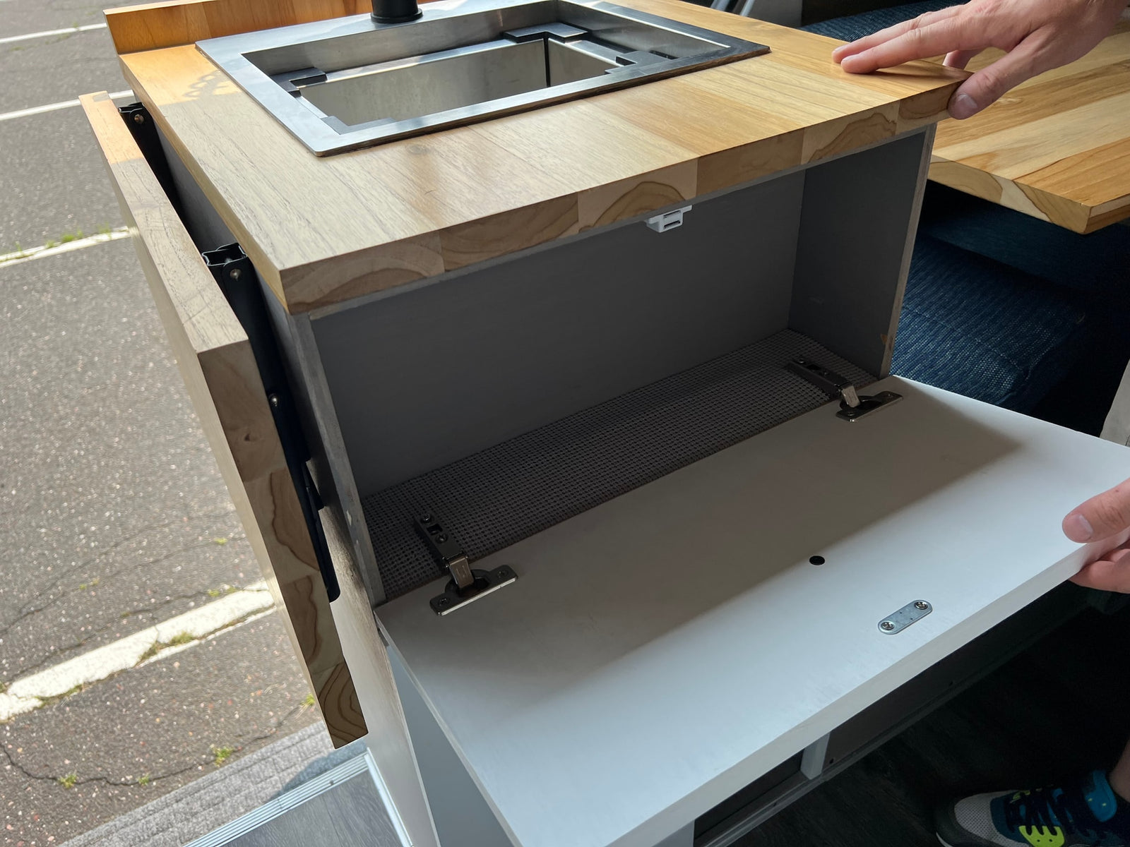 RV rental kitchenette: A wooden counter with an integrated sink and an open cabinet revealing organized storage.