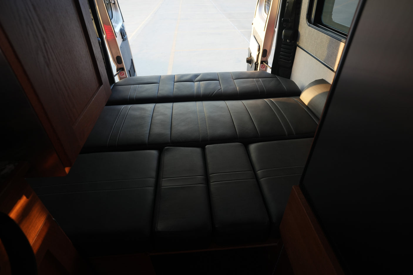 RV rental interior with a comfortable black leather bed/seating area, viewed from the front looking towards the open rear doors.
