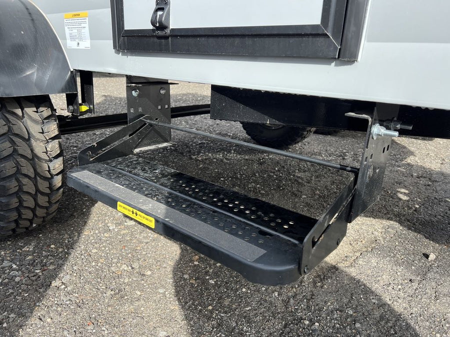 showcasing its deep treads and black rim.|A new Westlake Mud Legend spare tire is mounted on the front of an RV rental trailer