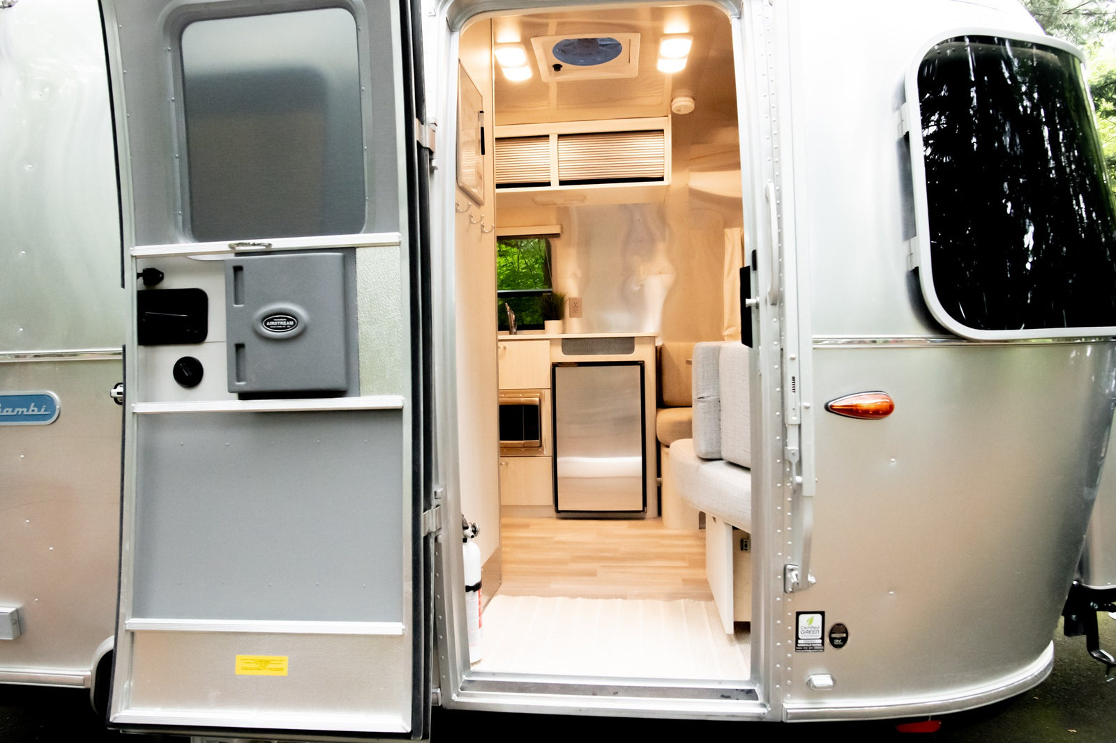 Open door view of a silver Airstream RV rental, revealing its modern interior with kitchen appliances & seating.