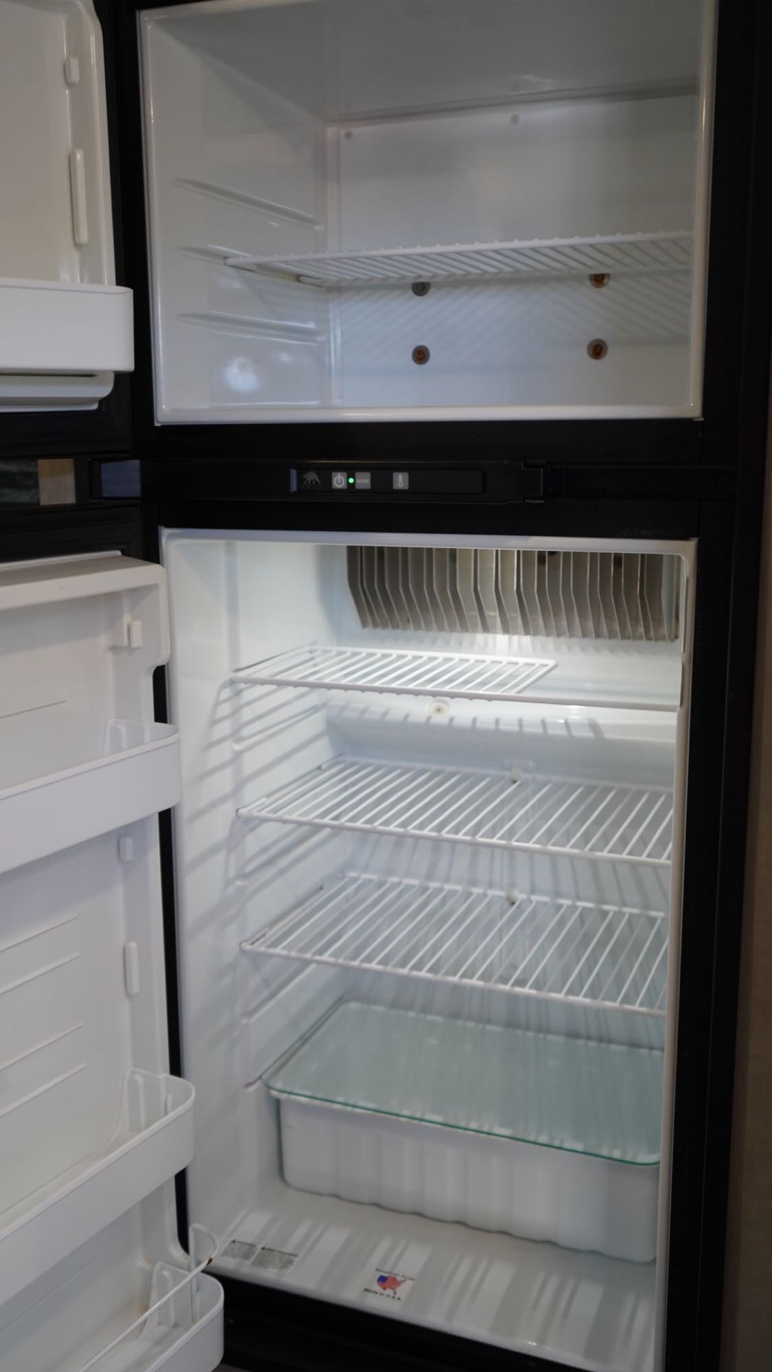 Clean, empty refrigerator and freezer interior, ideal for an RV rental. Features wire shelves and a crisper drawer.