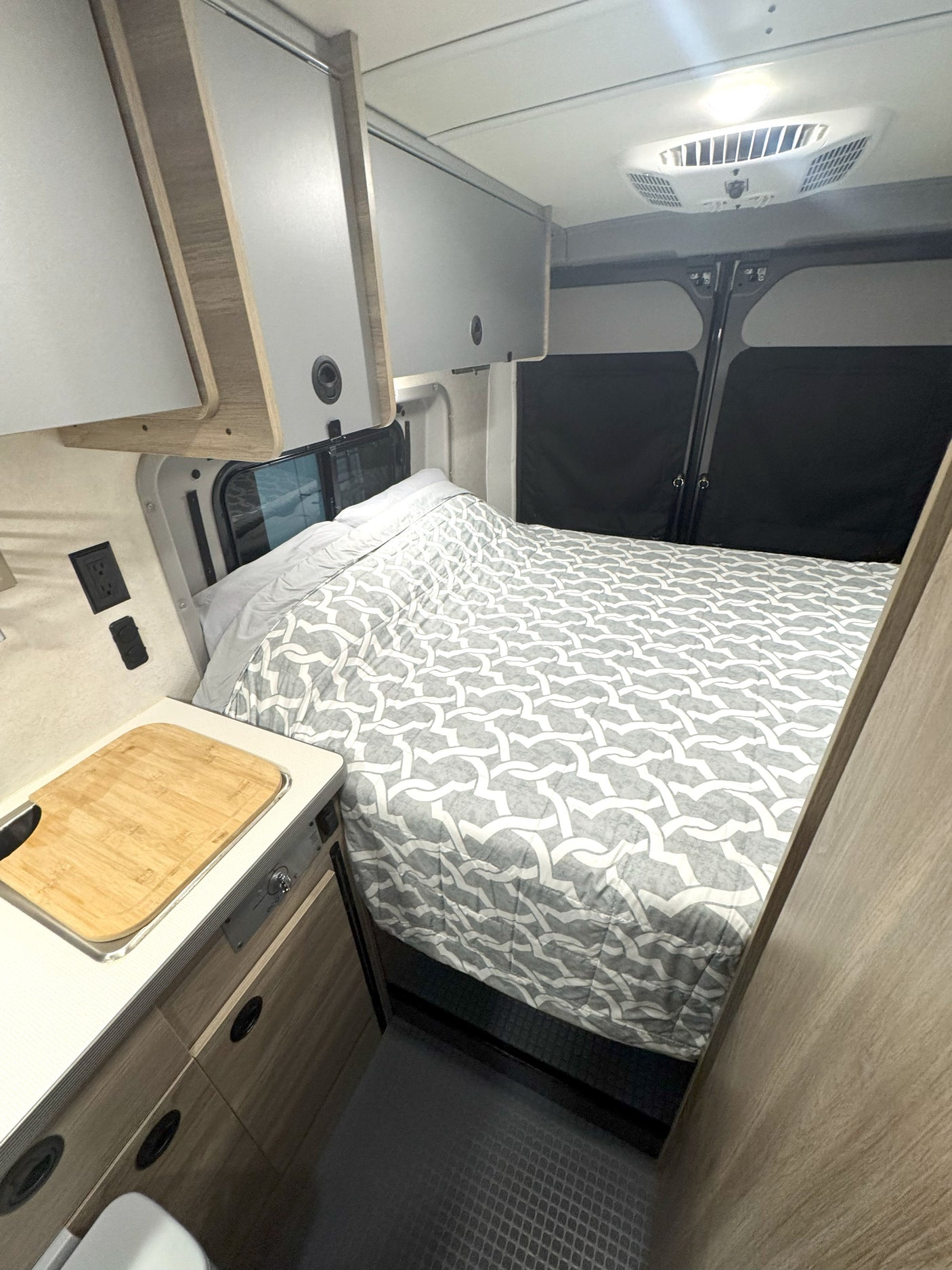Compact rv rental interior featuring a bed, kitchenette, and overhead cabinets for on-the-go living.
