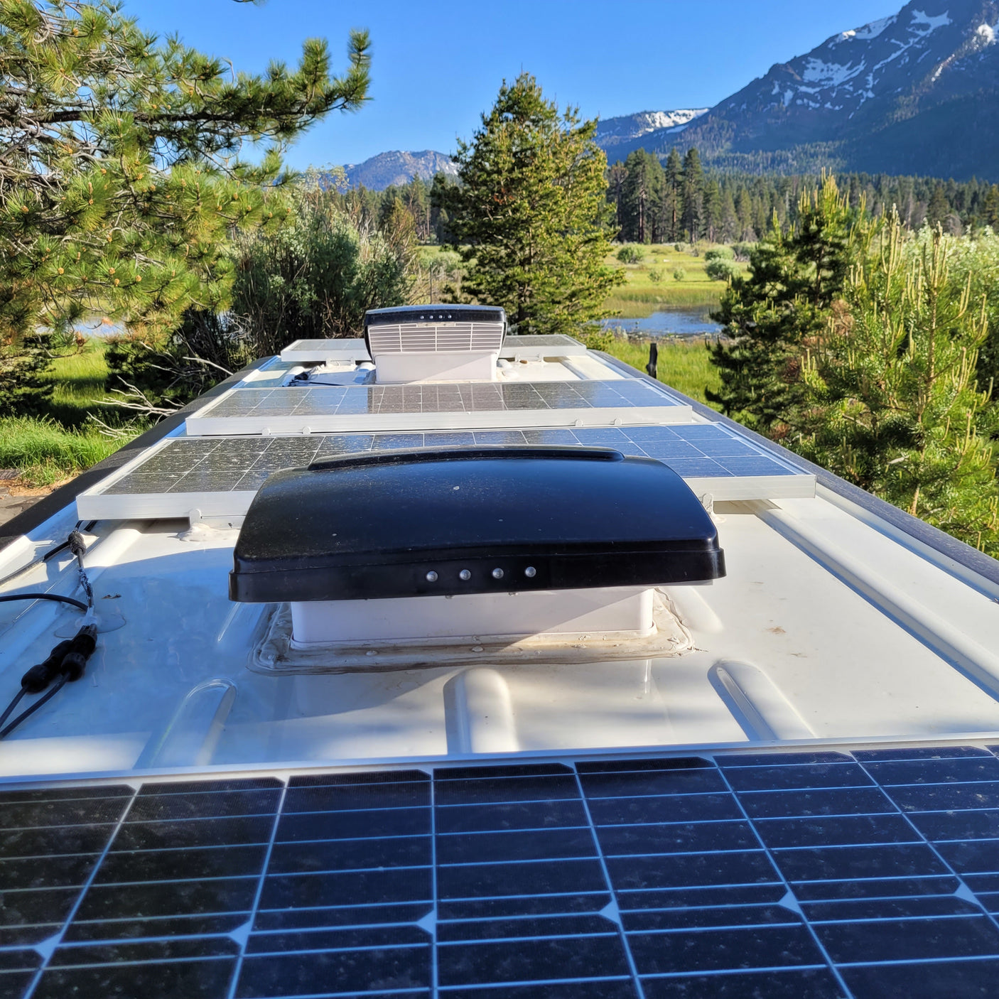 RV rental with solar panels and roof vents for off-grid adventure, set against a stunning mountain lake backdrop.