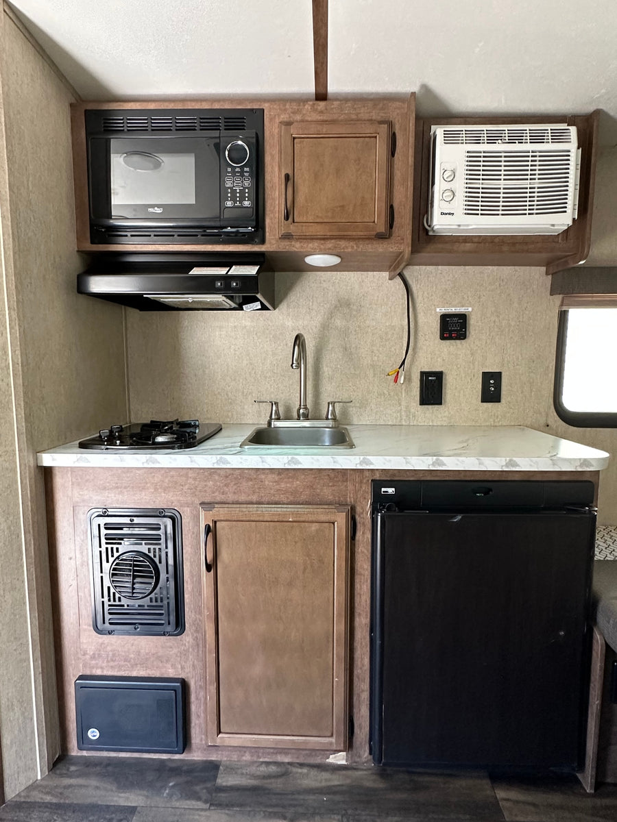 This RV rental kitchen features a microwave, stove, sink, fridge, and A/C, providing a full, compact setup.
