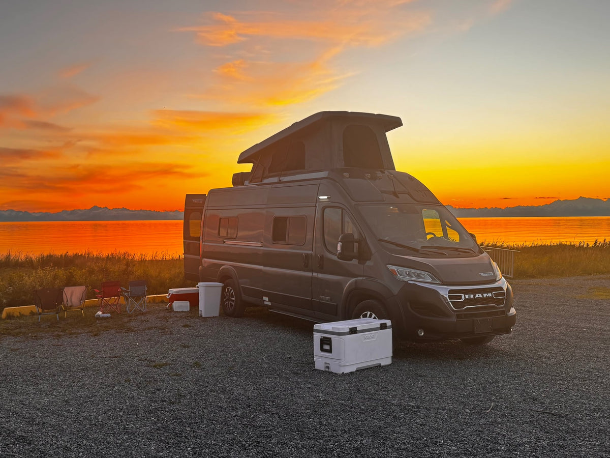 Experience your RV rental adventure! Camper van parked at a scenic waterfront campsite with a stunning sunset and mountains.|This gray Winnebago Solis rv rental