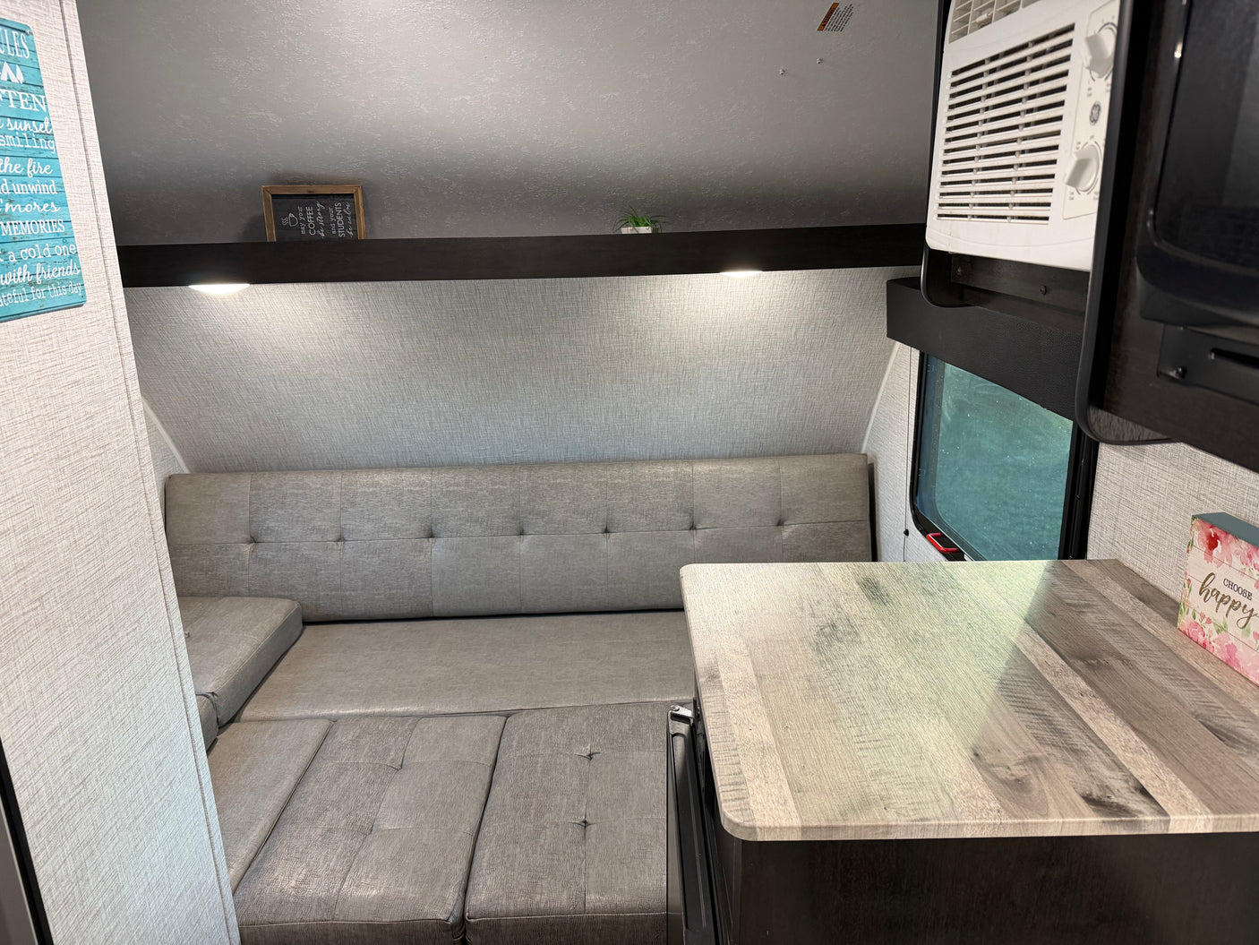 Cozy RV rental interior featuring a gray sofa-dinette, light wood-look countertop, and an AC unit for comfortable travel.
