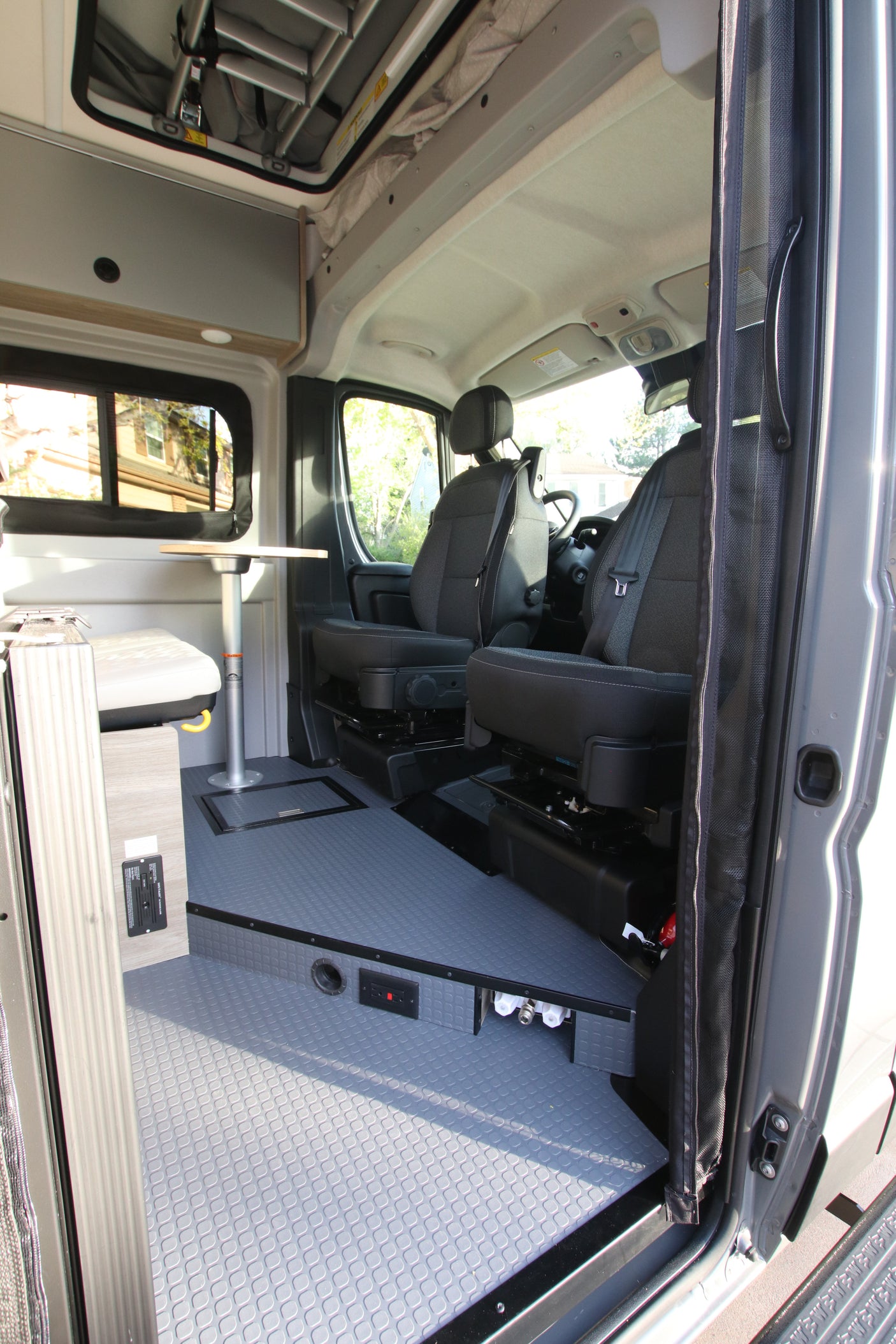 View into an rv rental camper van, showing the front seats, dinette table, and gray textured floor.