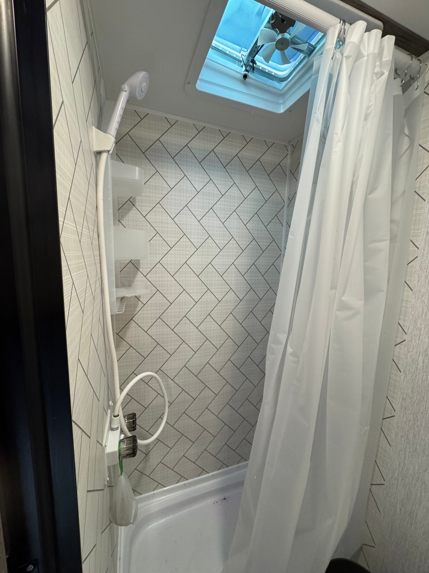 Inside an RV rental bathroom: a compact shower with a flexible shower head, a ceiling fan, and a white curtain.