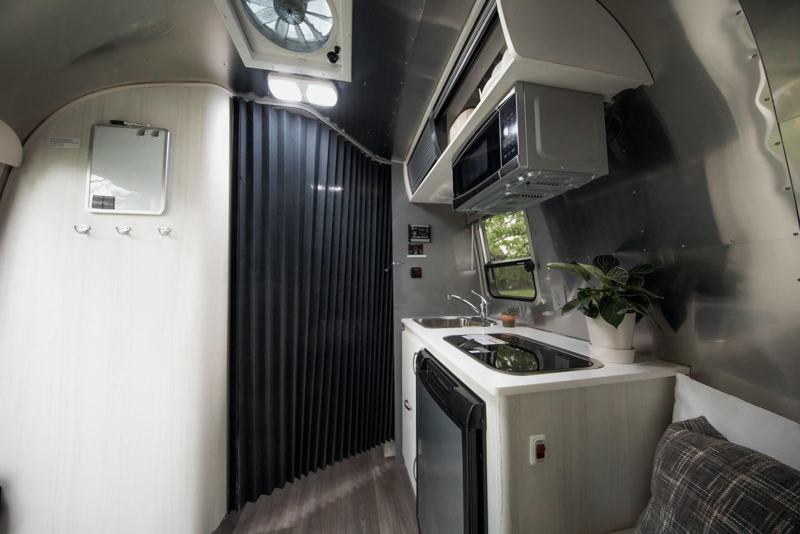 Inside a modern RV rental: a compact kitchen with microwave, sink, stovetop, and fridge, plus a flexible room divider.