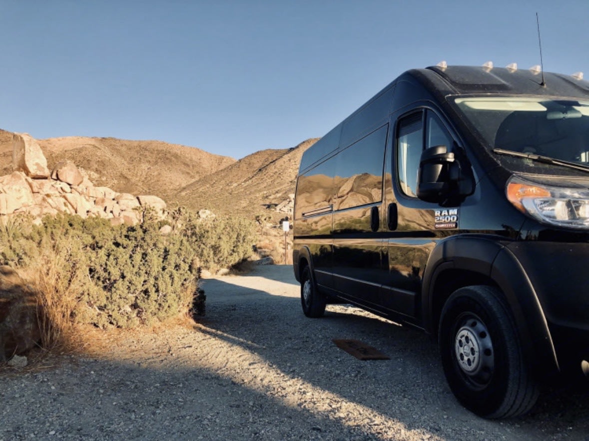 Black camper van RV rental parked on a desert road. Rocky mountains and clear sky reflected — photo 1