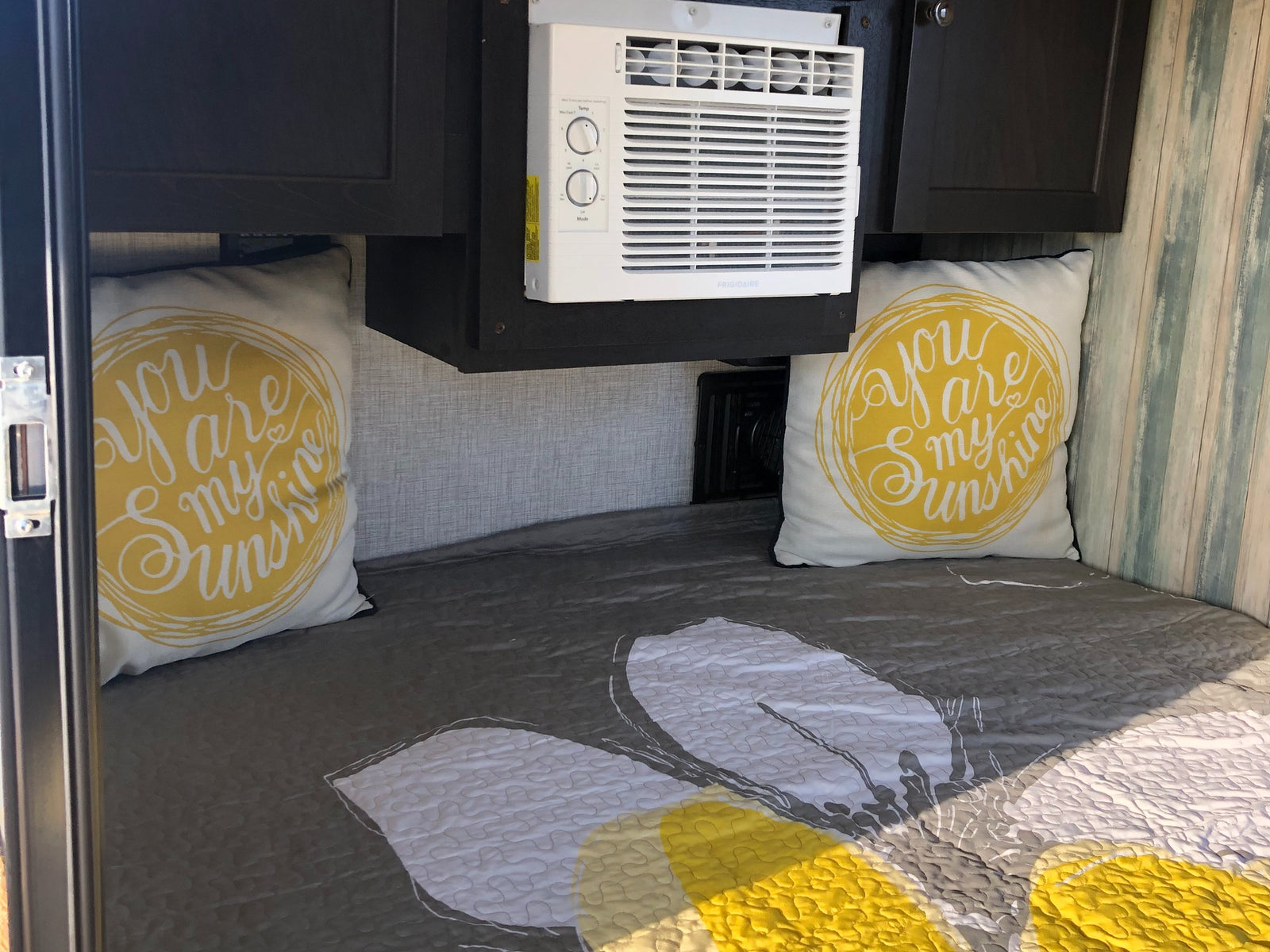 Cozy RV rental bedroom features a gray & yellow bed, "you are my sunshine" pillows, and an AC unit for comfort.