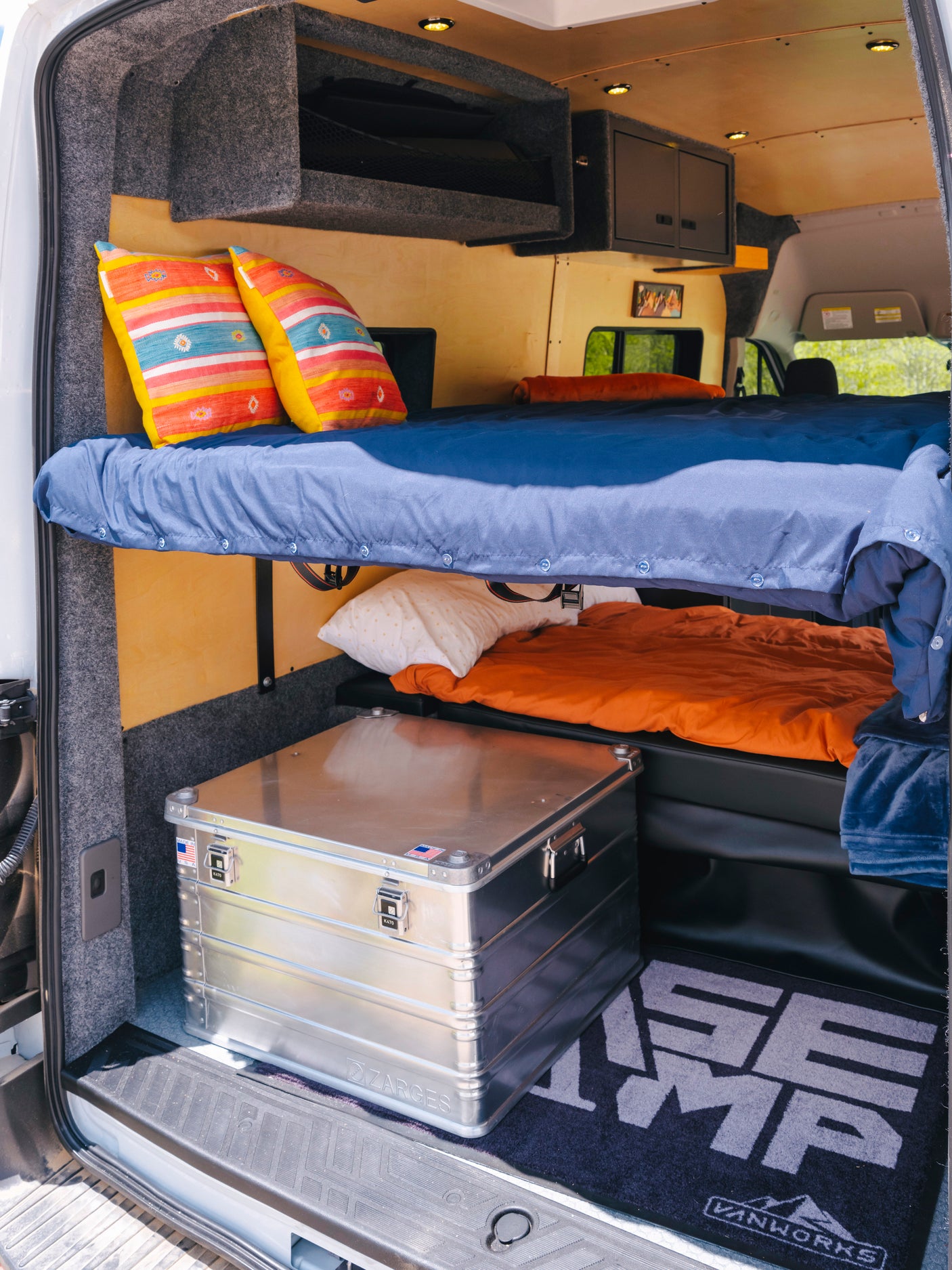 Spacious RV rental interior featuring two bunk beds with colorful pillows, overhead storage, and an aluminum gear box.