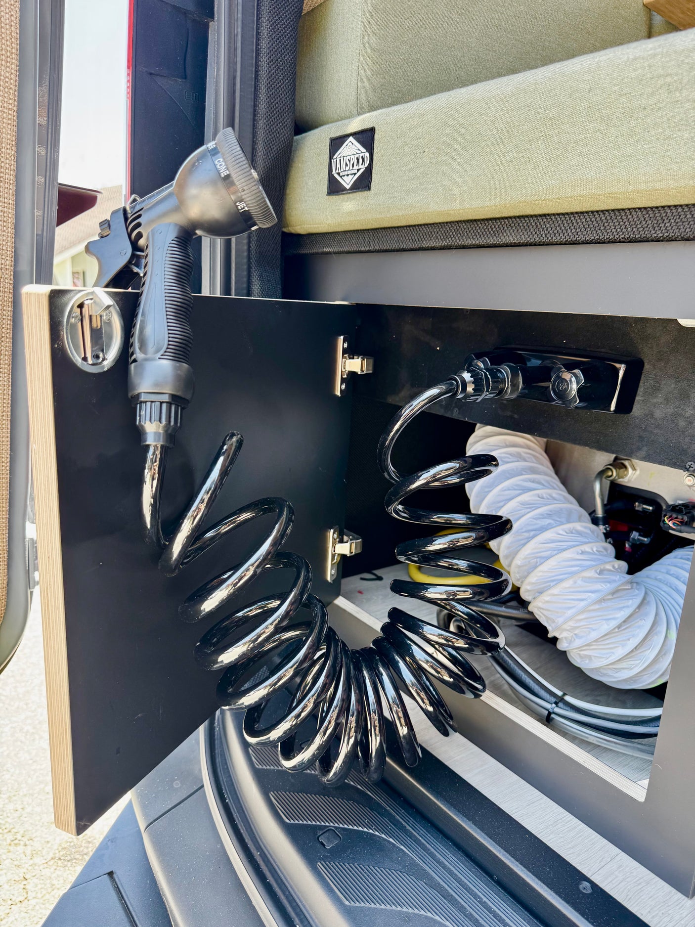 RV rental: A camper van's compact outdoor shower with coiled hose and nozzle, neatly stored inside a side cabinet.