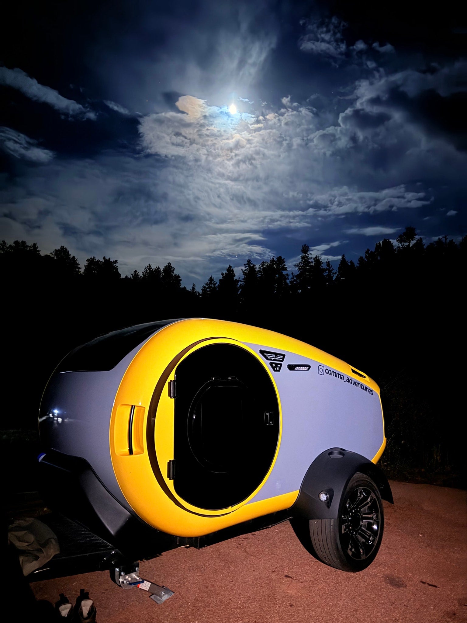 Unique yellow and grey camper trailer RV rental, glowing under a moonlit sky. Ready for adventure!