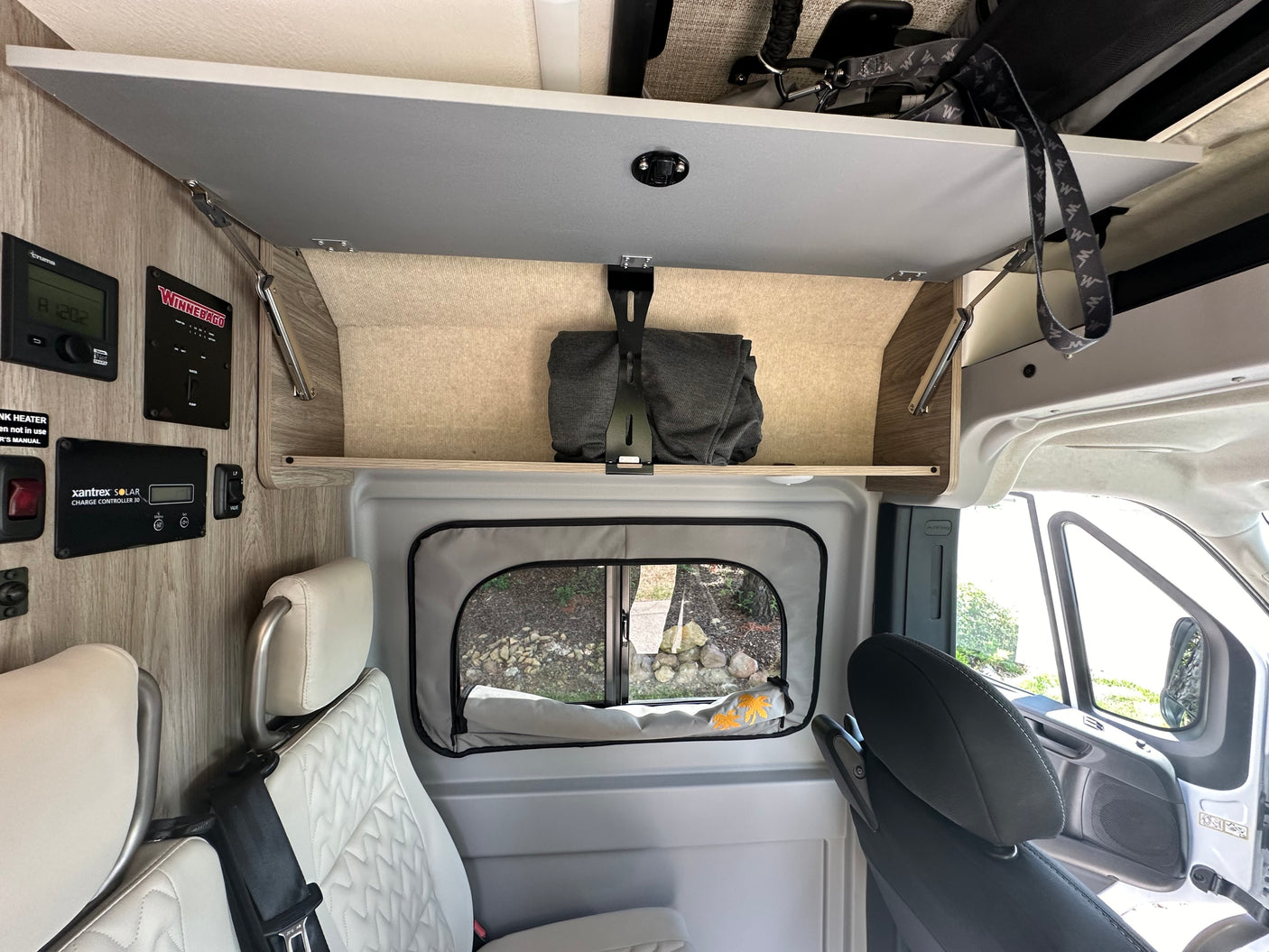 Inside an RV rental, showing control panels for Truma, Winnebago, Xantrex Solar, overhead storage, and comfortable seats.